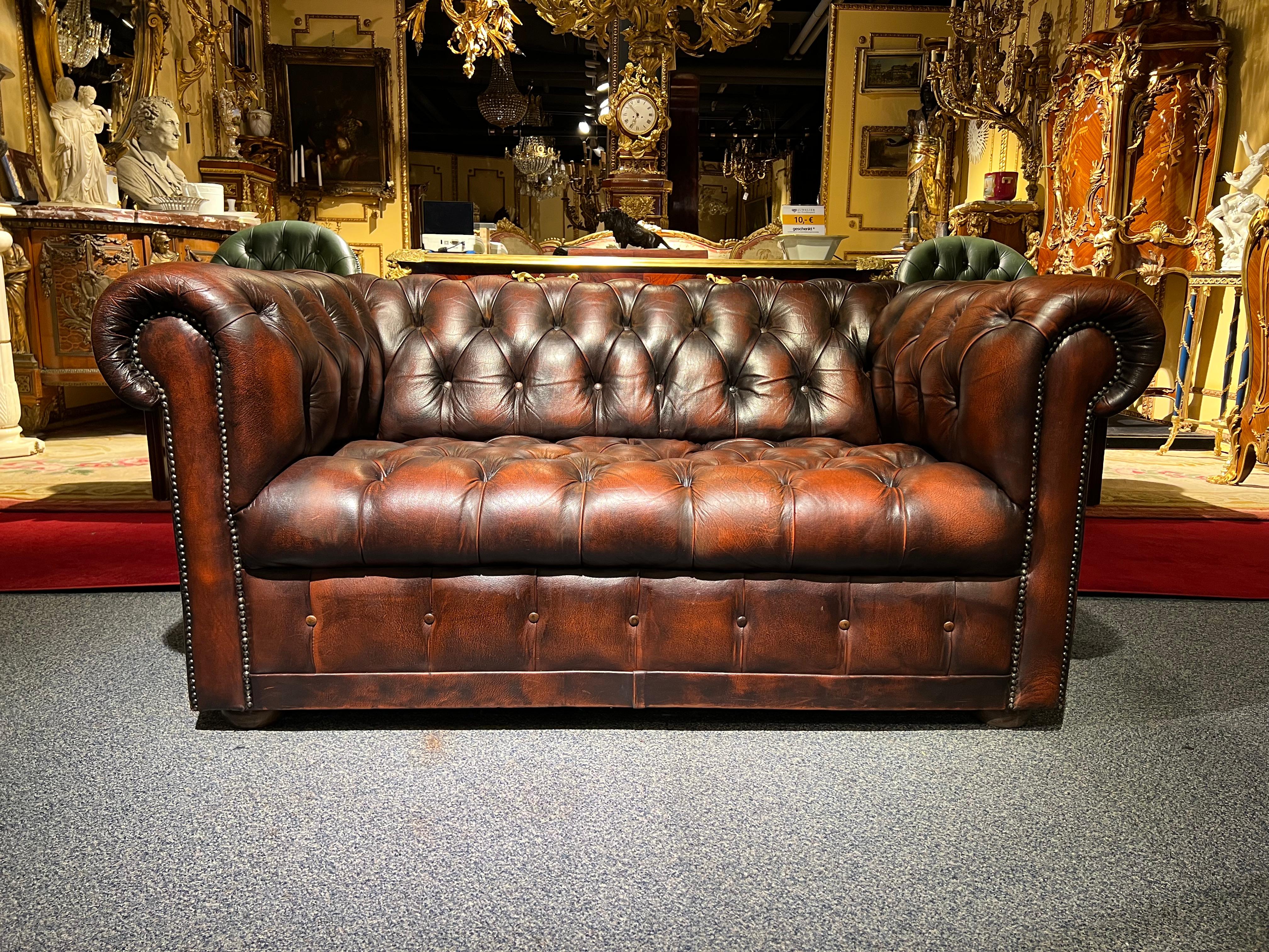 2-seat chesterfield sofa with button tufted detail. Exceptional quality. Double hand-stitching, and applied brass nailhead trim details. The ebonized composite orb feet have been left original, showing wear from age / use. The leather is aged