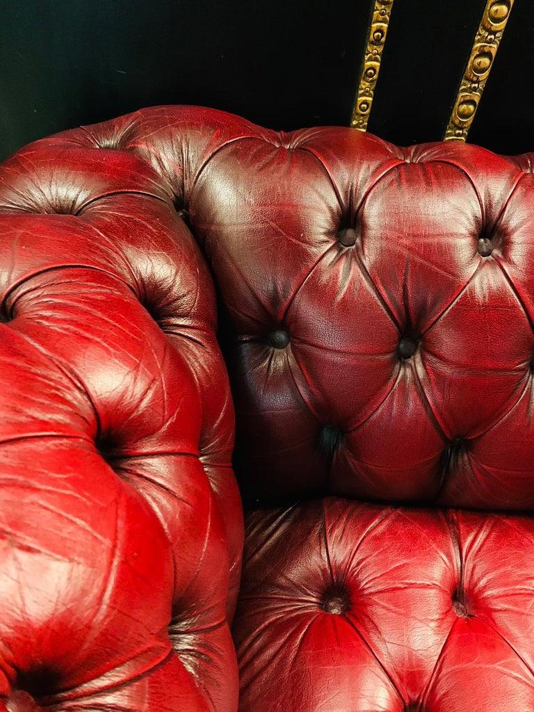 2-seat chesterfield sofa with button tufted detail, circa 1970. Exceptional quality. Double hand-stitching, and applied brass nailhead trim details. The ebonized composite orb feet have been left original, showing wear from age / use. The leather is