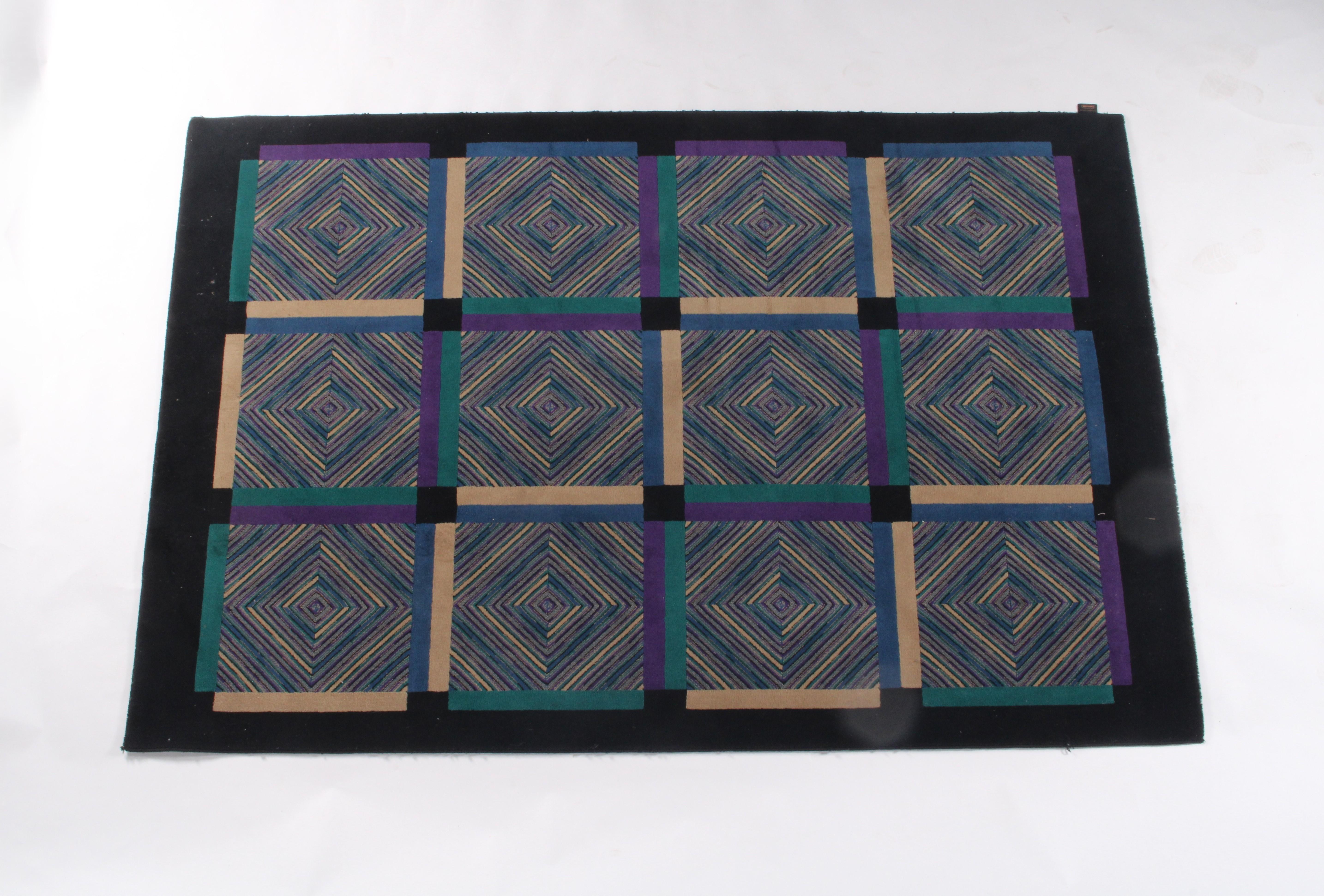 Esta alfombra vintage de Missoni, un sorprendente ejemplo del diseño italiano de los años 80, está confeccionada en pura lana virgen y muestra la icónica maestría de la marca en cuanto a estampados y colores. La composición presenta una retícula