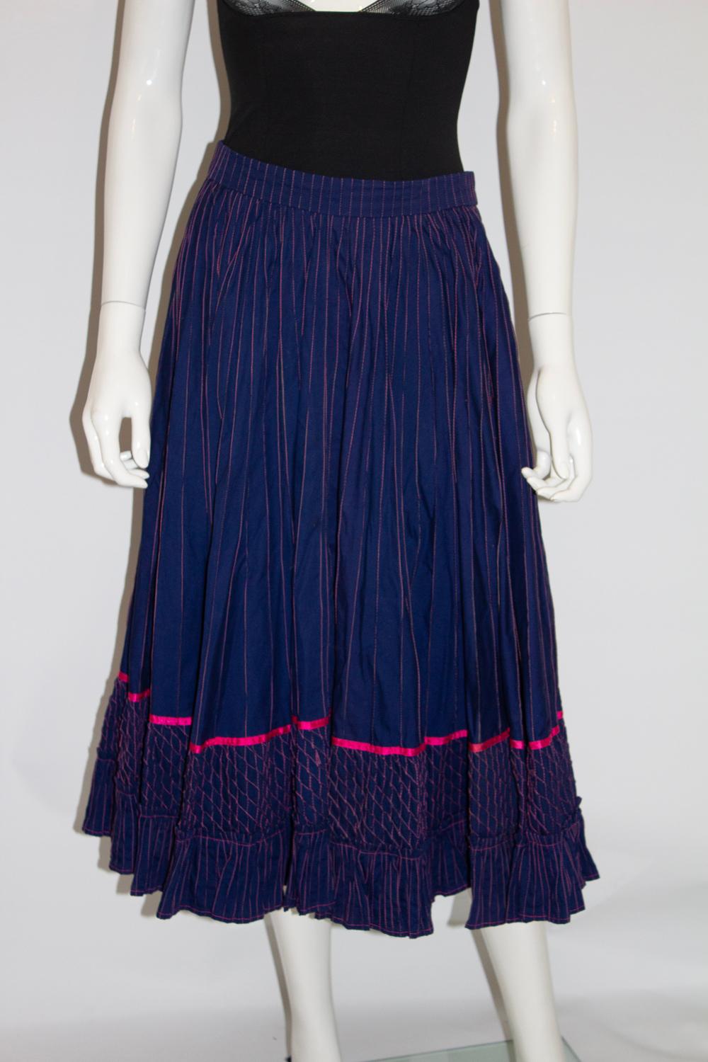 Une superbe jupe vintage de la marque Mexicana des années 1970. La jupe est en coton bleu foncé avec des points de couture roses. Il est froncé à la taille et son ourlet est orné d'un ruban rose et de points de couture. Il n'est pas doublé et est en