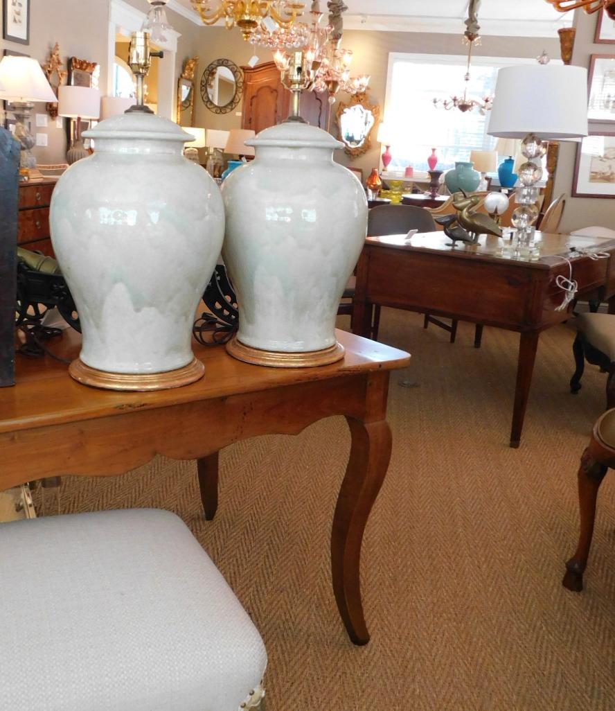 Each large ginger jar with subtle celadon drip glaze with fine craquelure to surface, raised on turned giltwood bases, measures: 18.5