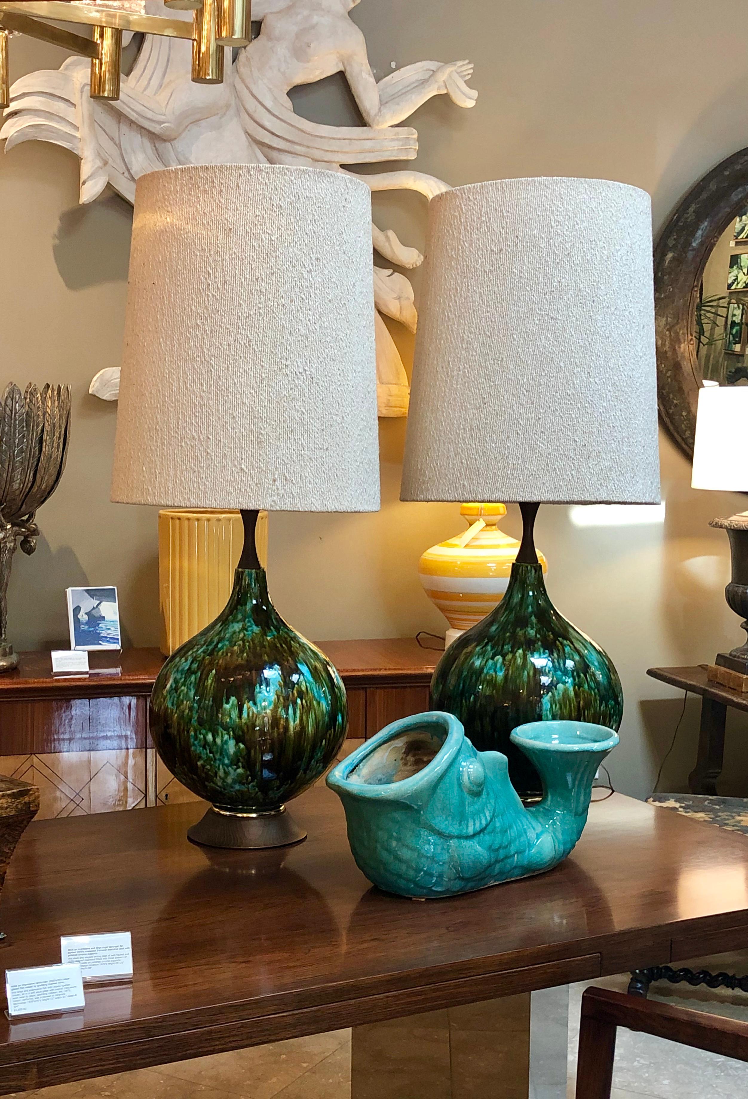 1960s glam at its best, each of large bulbous form covered in a rich olive green and teal drip-glaze, resting on a splayed wooden base with brass perimeter band.