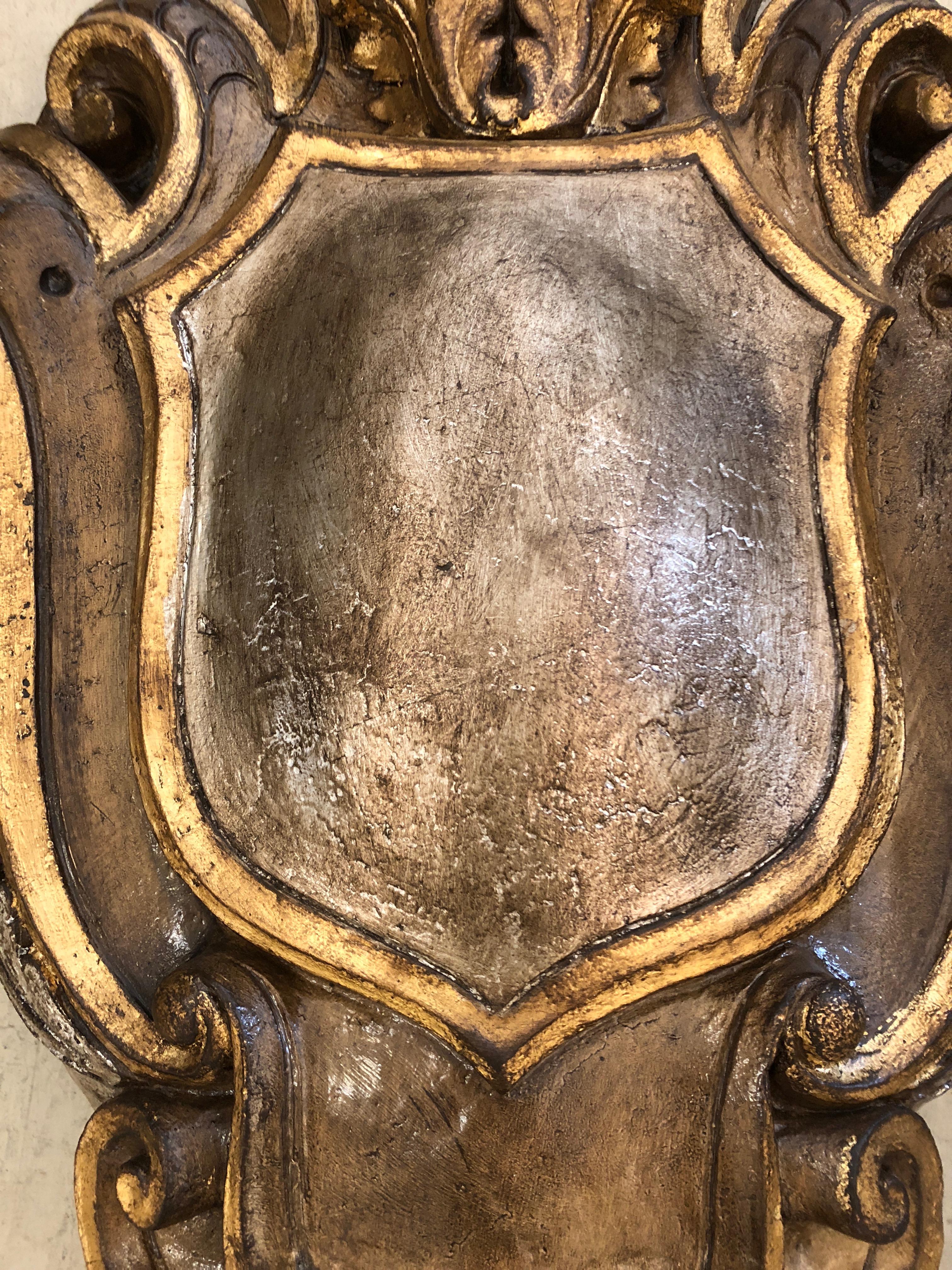 A superbly impressive large found object in the shape of a medieval shield, painted gold and silver. 
Would look amazing over a mantle. A true focal point.