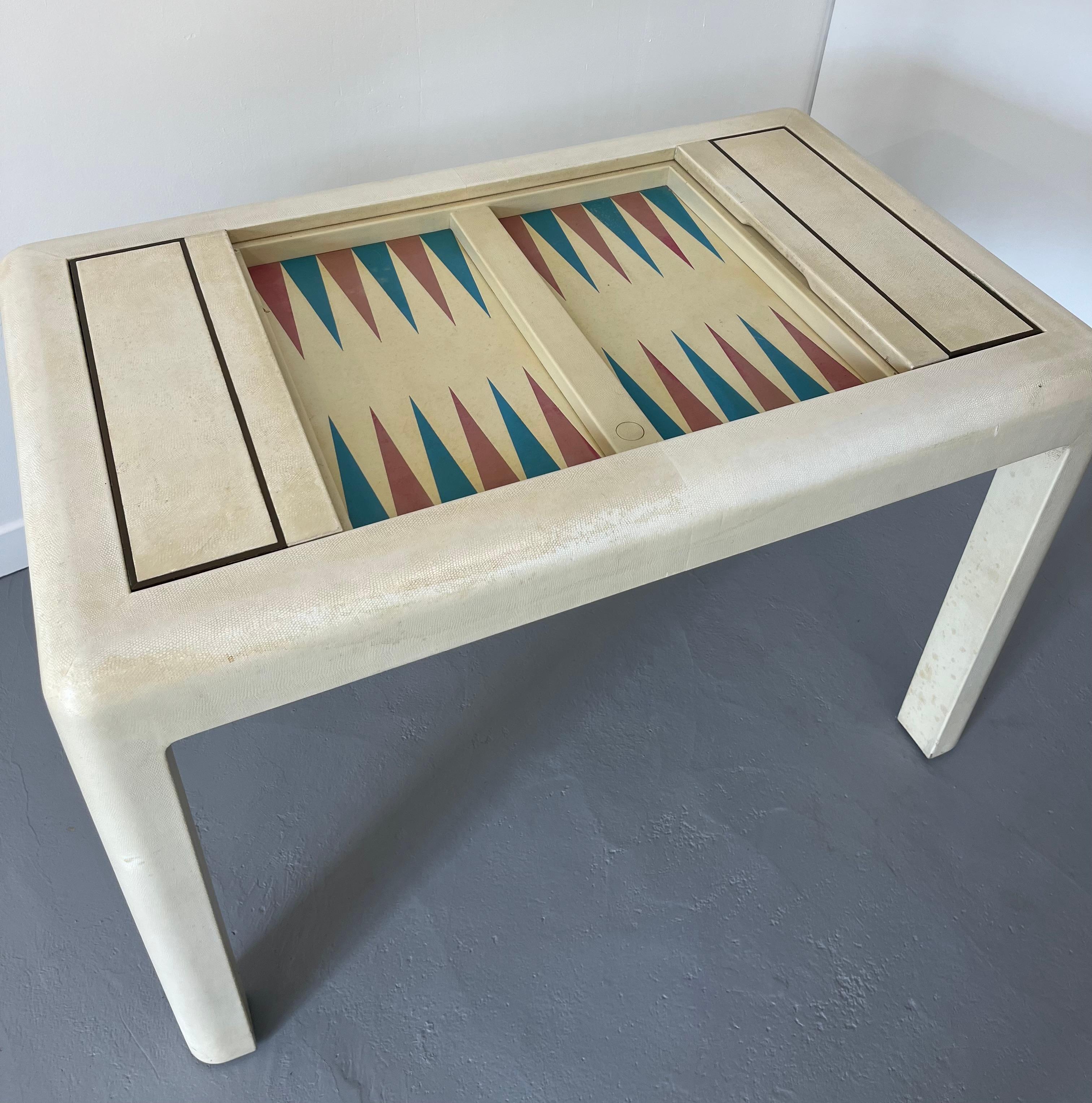 Wood Table fully wrapped in ivory beige snakeskin revealing two backgammon boards and two hinged side compartments housing four die, two dice cups in conforming snakeskin,  and thirty checkers in brown and white of marble resin.
One small default on