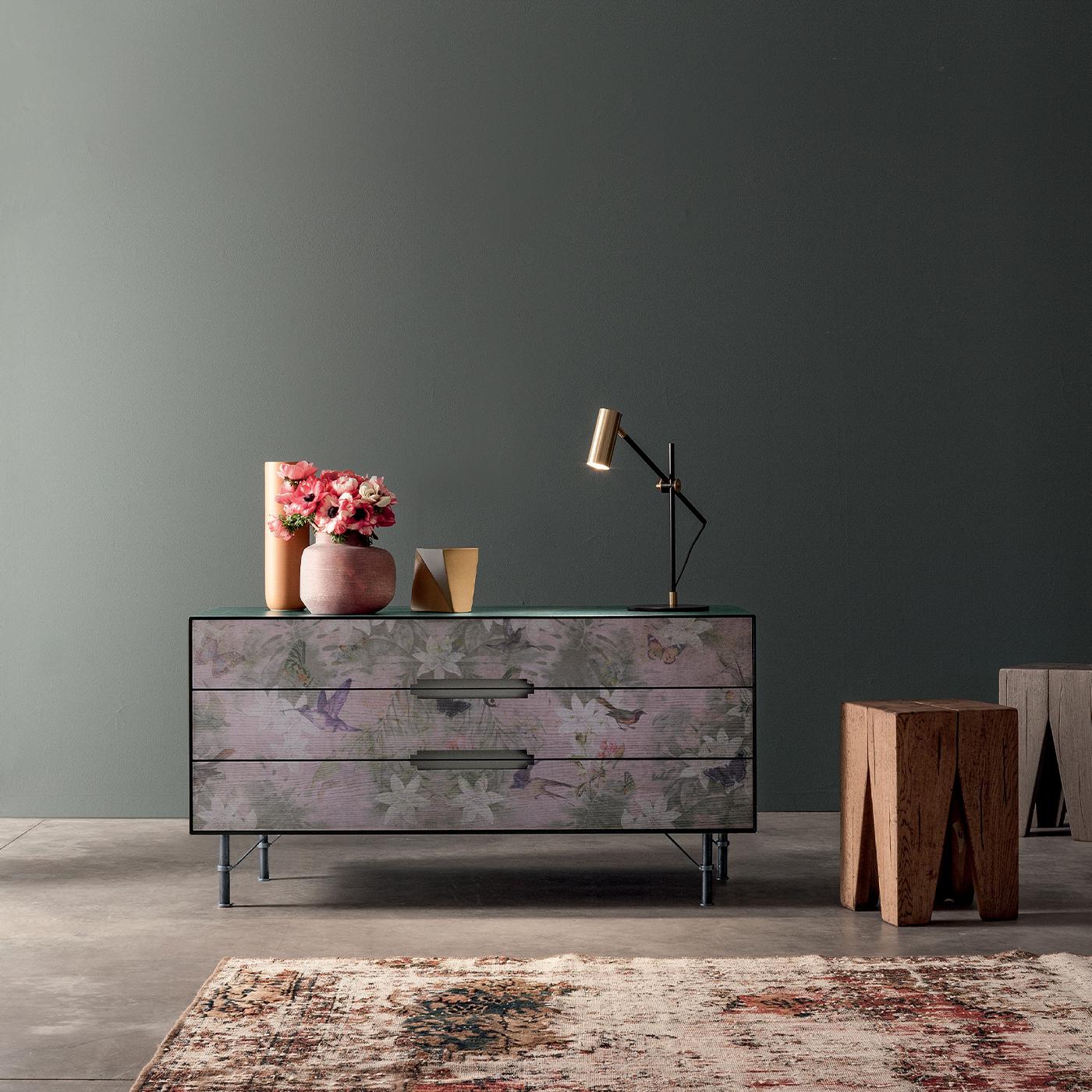 This long chest of drawers updates a Classic style with a stunning printed front, complete with flowers and birds in warm dusty hues. Its three drawers provide ample storage space, opening with sleek cutout handles. Finished with iron feet for a
