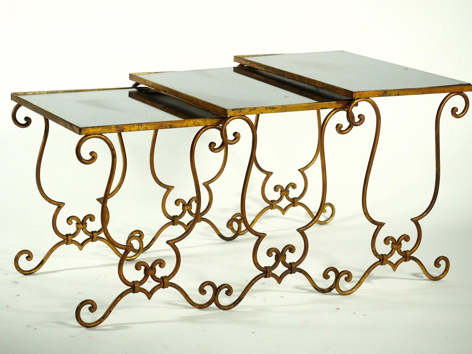 French 1940s Art Deco set of three stack or nesting tables in the style of Jean-Charles Moreux. Gold leafed forged iron with original distressed mirror tops.