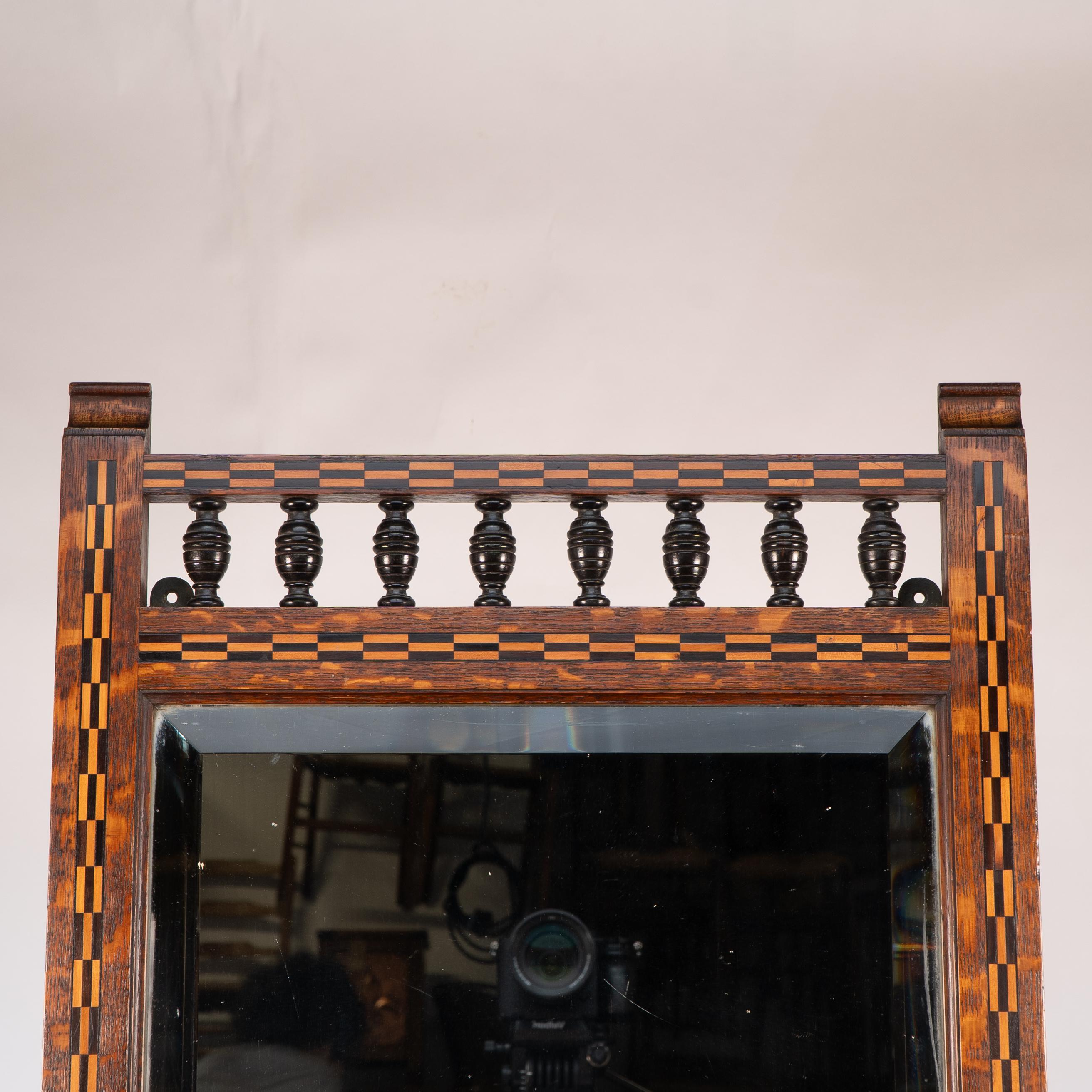 Shapland and Petter attributed. In the style of M H Baillie Scott an A&C oak mirror with chequer inlays of ebony and box wood with a lower shelf and shaped supports, Scroll finials and ebonised turnings to the top.