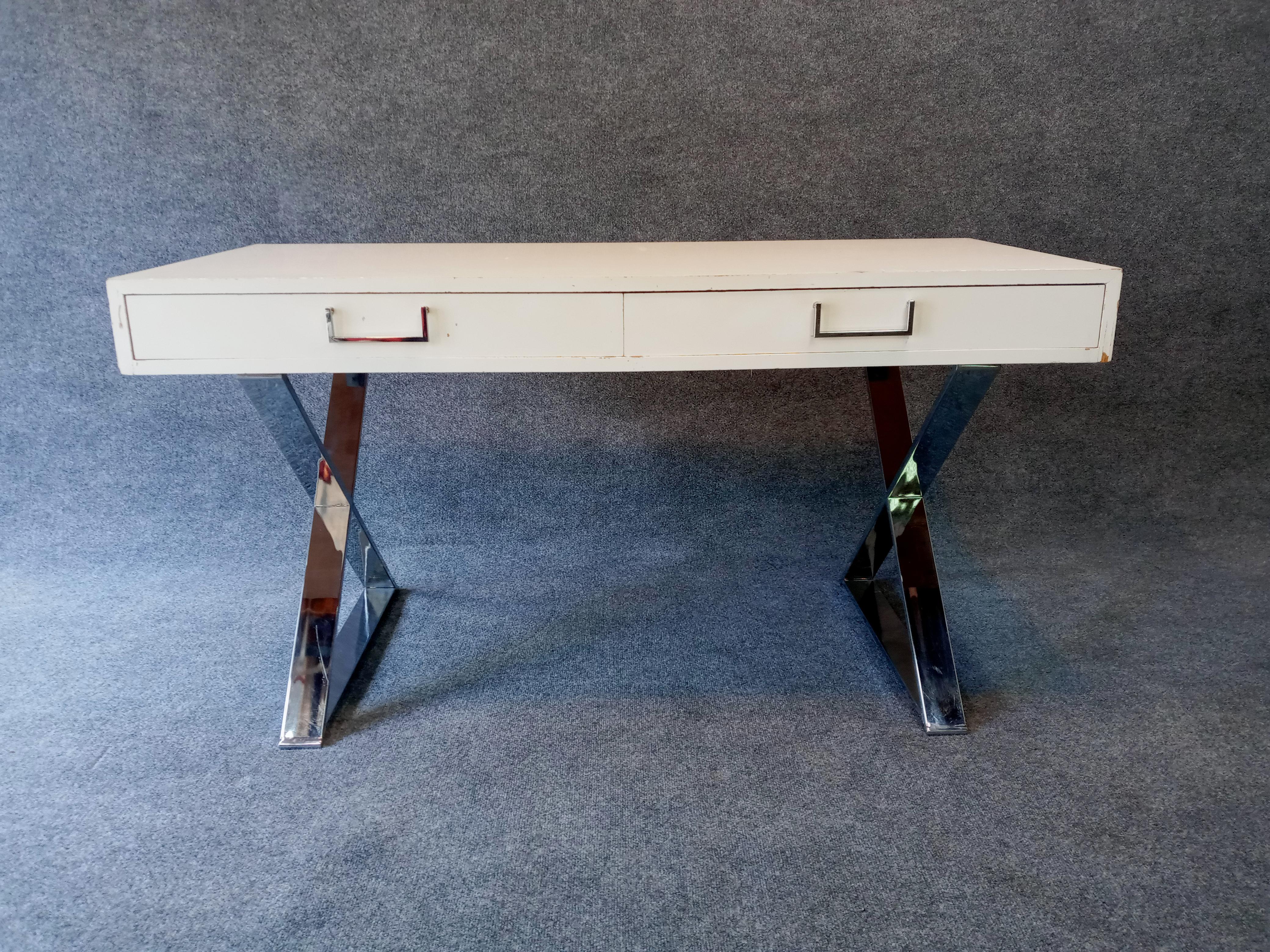 Retailed by John Stewart, heavily influenced by the designs of Milo Baughman. This modest-scale desk features two drawers and has original finishes intact. The original white enamel shows age appropriate scuffs, scratches, and signs of general wear.
