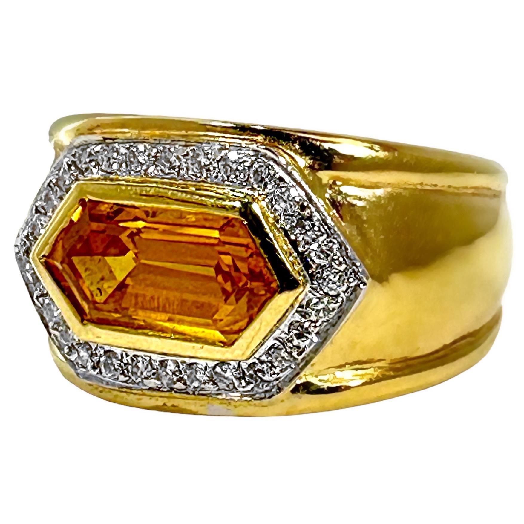 This striking 18k yellow gold 1980's cocktail ring is bezel set, east to west, with one elongated, golden orange, hexagonal cut, natural sapphire*. Surrounding this vivid stone is a pave' plate set with twenty six round brilliant cut diamonds. The