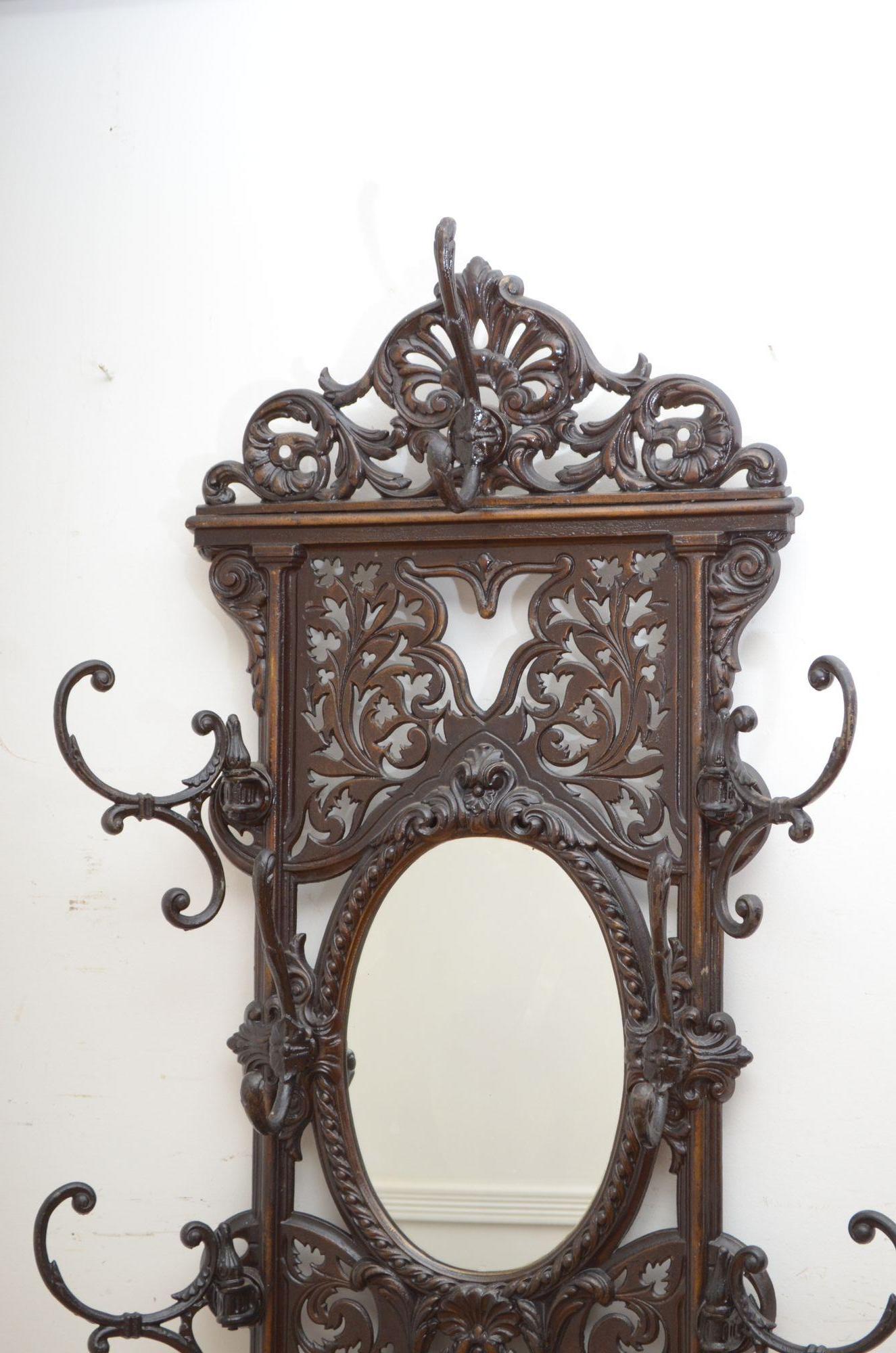 P0269 Attractive cast iron hall stand having six coat and hat hooks, four of which swivel, original oval mirror, umbrella and walking sticks compartments and original enamelled removable drip tray, The hall stand is decorated with pierced detail