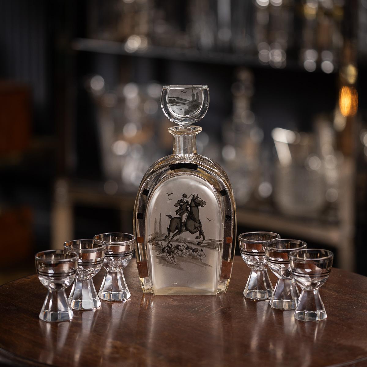 Carafe en forme de fer à cheval du 20e siècle, gravée d'une scène de chasse en monotones sur le devant. L'ensemble est complété par six verres, chacun avec des rayures noires et argentées, et un socle en verre taillé. Ce set constitue un objet de