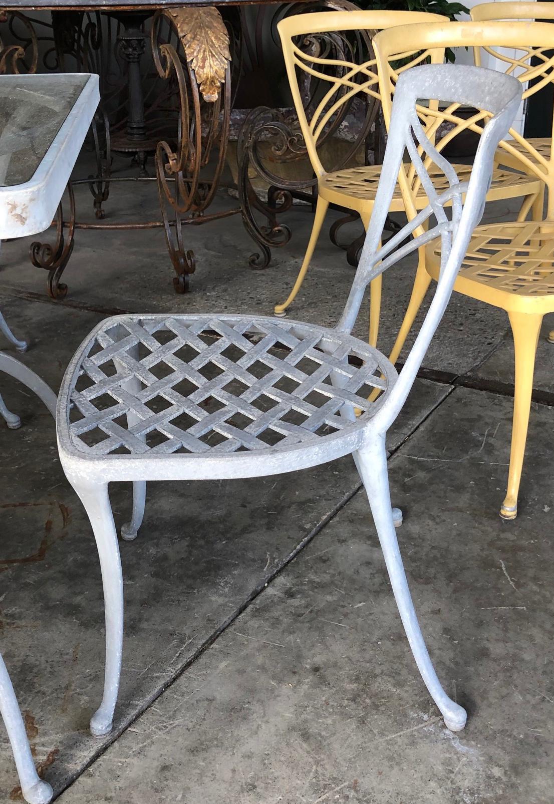 A stylish American 1960s five piece aluminum patio set with square glass-top and 4 side chairs; by Brown Jordan; the square table on down-turned legs; with 4 graceful side chairs with open trellis-work seats over splayed supports; structurally