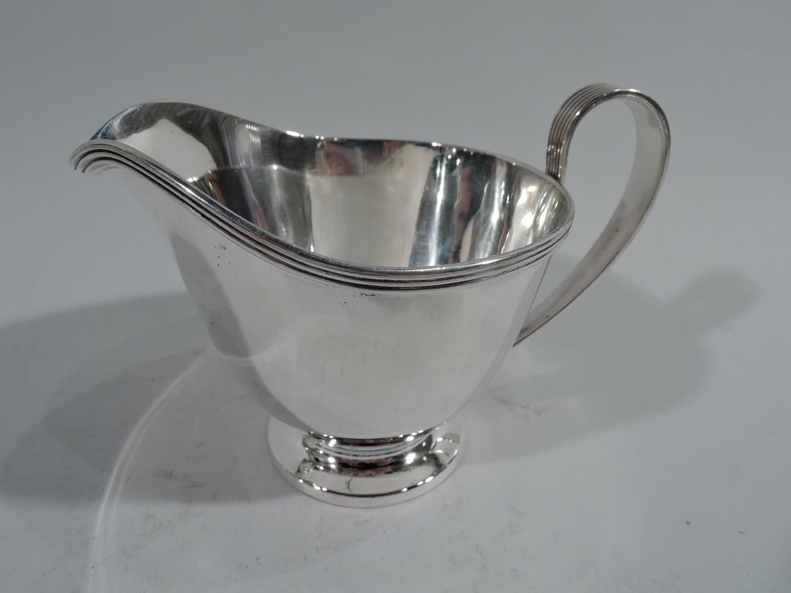 Stylish sterling silver creamer and sugar. Made by Tiffany & Co. in New York. Each: Round on raised foot. Creamer has soft lip spout and high-looping handle. Sugar has c-scroll swing handle. Handles tapering and reeded as are rims. Hallmarks include