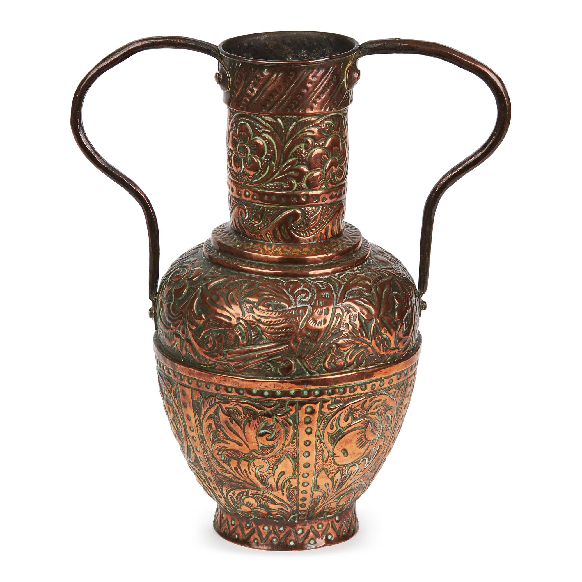 A stylish antique Asian twin handled copper vase decorated with repousse designs. This elegantly made vase, either of Indian or Middle Eastern origin is decorated with panels containing floral and bird designs with thin solid handles applied to