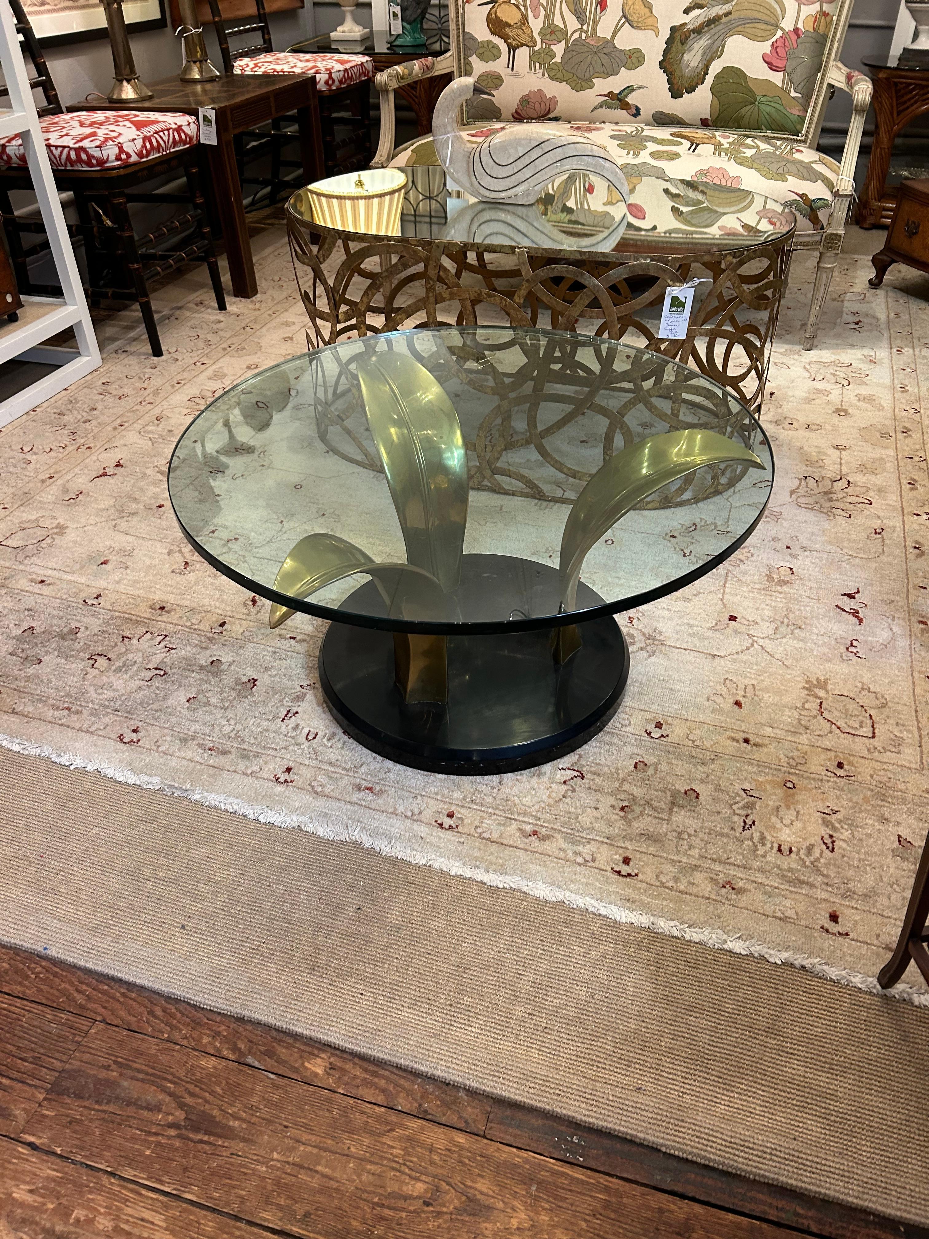 Sophisticated art deco style round coffee table having trio of brass palm leaves supporting 1” thick glass top.  The black stone base contrasts beautifully with the gold of the leaves.