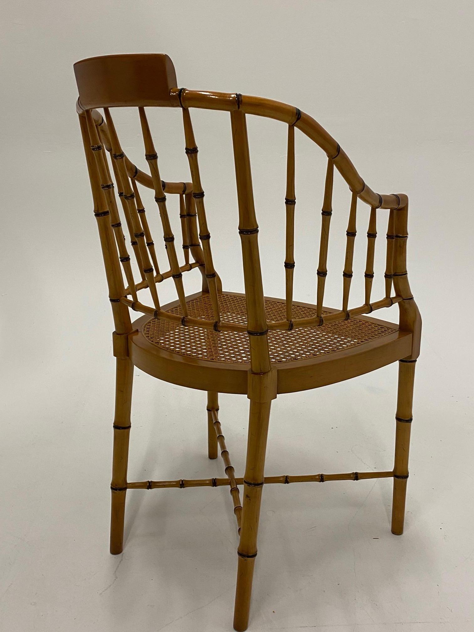 Great looking Regency armchair by Baker having faux bamboo frame, curved back with spindles and wonderful faux bamboo stretcher to match. Seat is a handsomely caned.