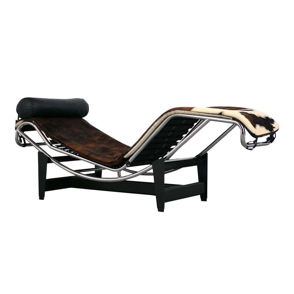 This Vintage LC4 Le Corbusier style Chaise Lounge features a tubular chrome frame that rests on top of the black enamel metal base. The chaise is upholstered in a brown, white, and black color cowhide and also features a black leather headrest
