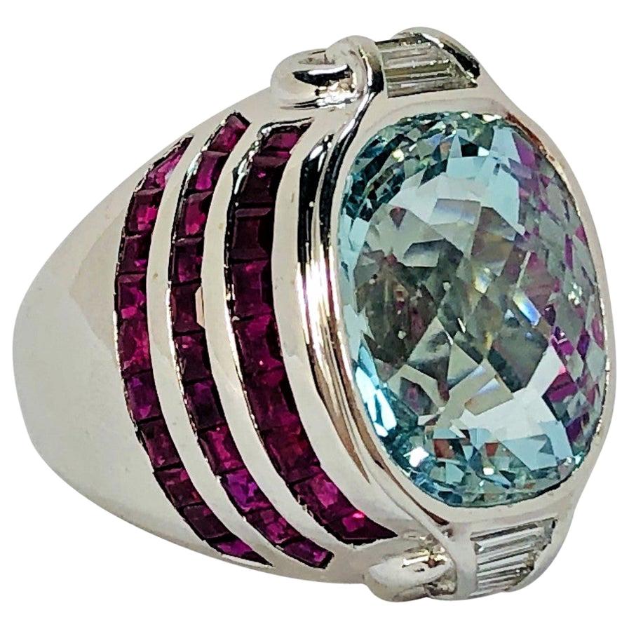 An oval shaped, checkerboard faceted aquamarine in the center,  with three rows of square, step cut rubies on each side, and with four straight baguette diamonds above and four below, set in an 18K White Gold mounting. The aquamarine weighs