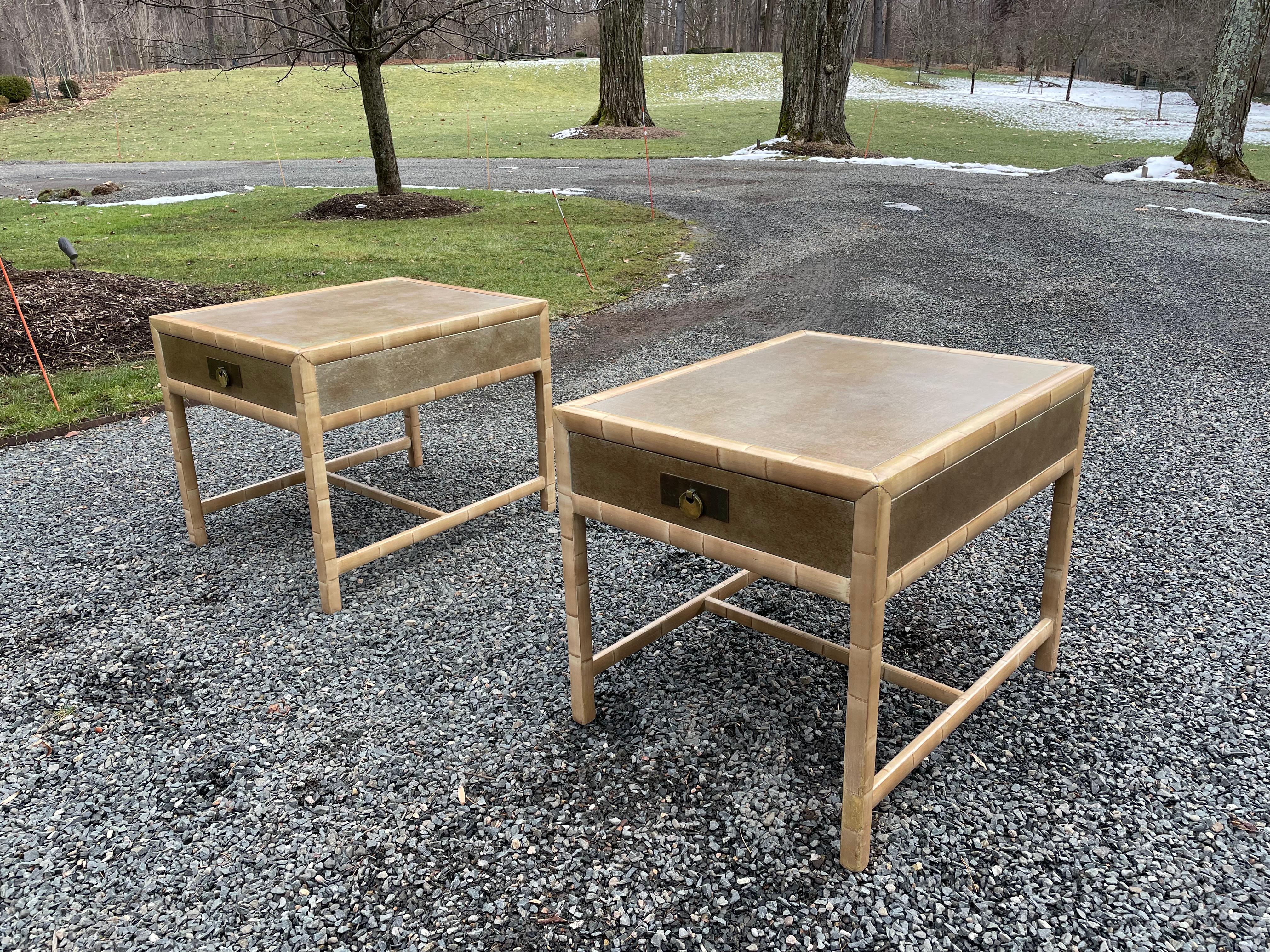Stunning pair of faux bamboo single drawer side tables or night stands by Baker. Tables have exposed wood frames and gilt textured tops with brass plaques and ring handles.
