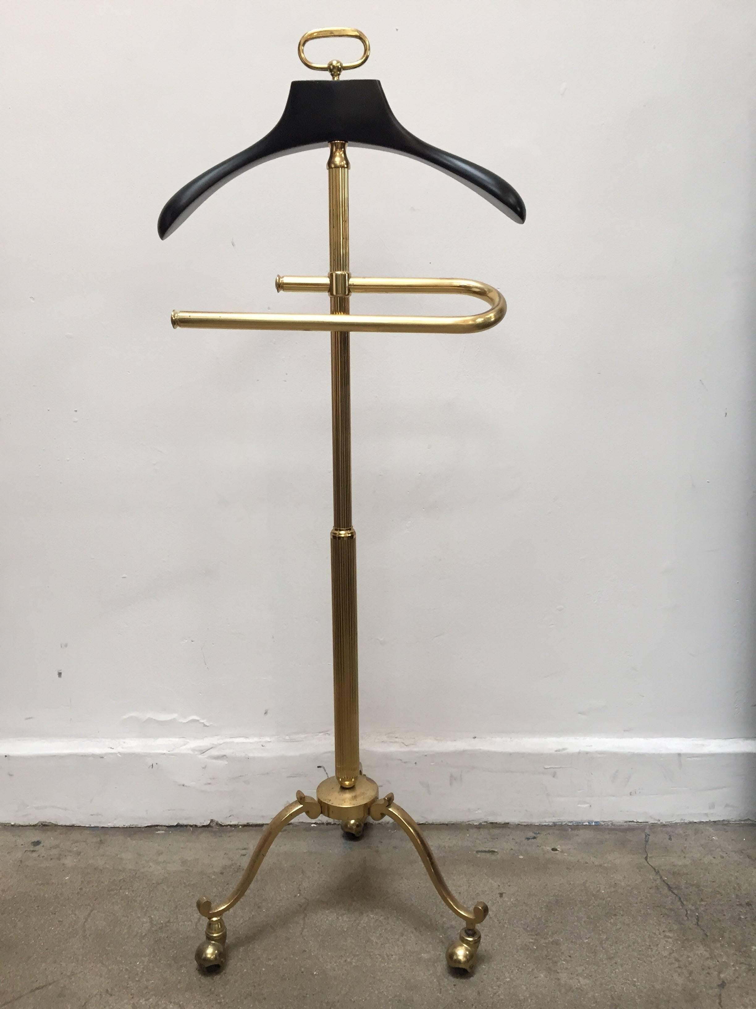 Stylish Italian gentleman polished brass glamorous valet stand.
Impressive Mastercraft polished brass valet stand, with a wooden coat holder and brass pants holder and brass change and jewelry holder on ornate tripod legs.. 
On caster base.