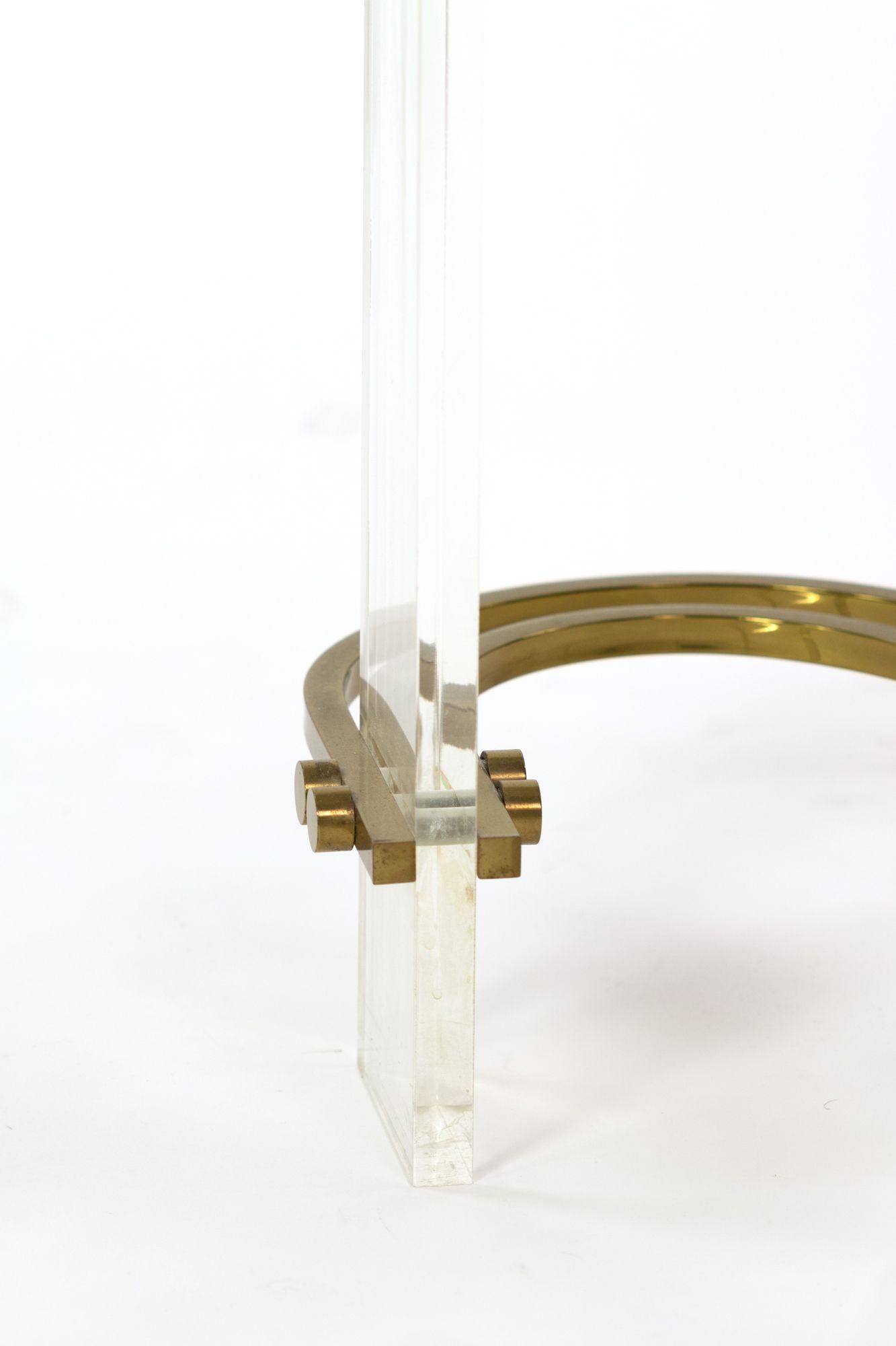 The kidney-shaped glass top raised on 3 rectilinear Lucite supports all joined by curvaceous brass stretchers.