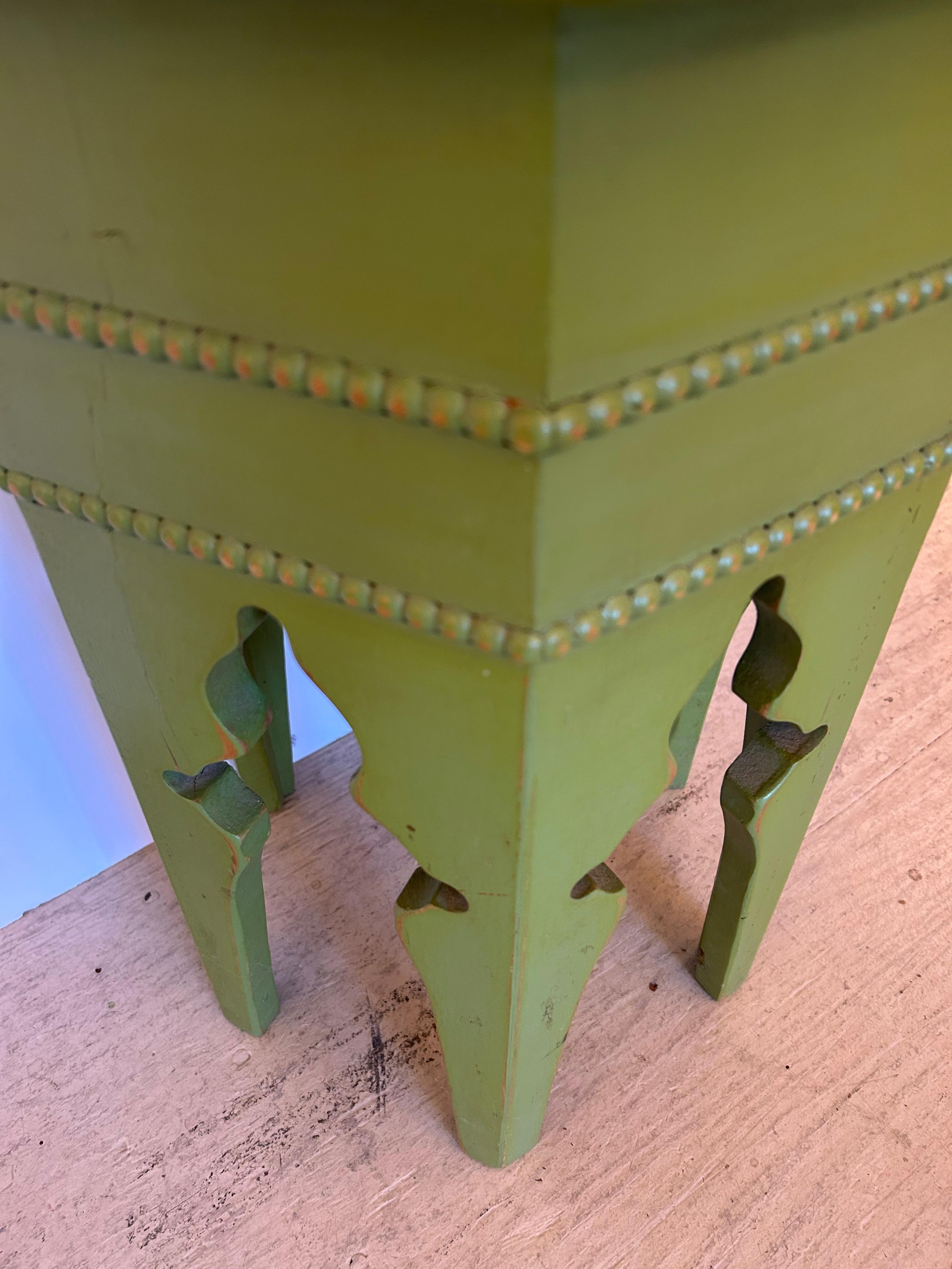Elegante mesa auxiliar de madera pintada de color verde sopa de guisantes, de aire marroquí, con tablero hexagonal, patas de forma morisca y detalles de cuentas en relieve.