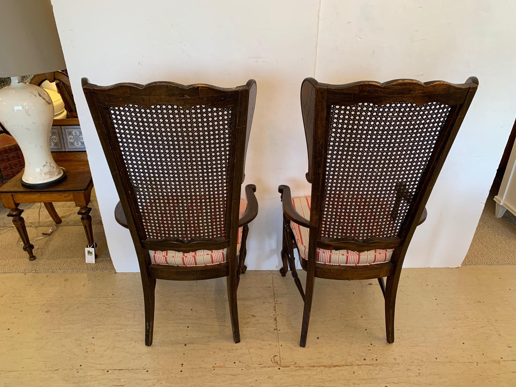 Stylish versatile pair of walnut armchairs having elongated caned back with scalloped top and side wings that flair out. Seat is upholstered in a light green and burnt orange striped fabric. Handsome curvy stretchers and snail shaped feet. These