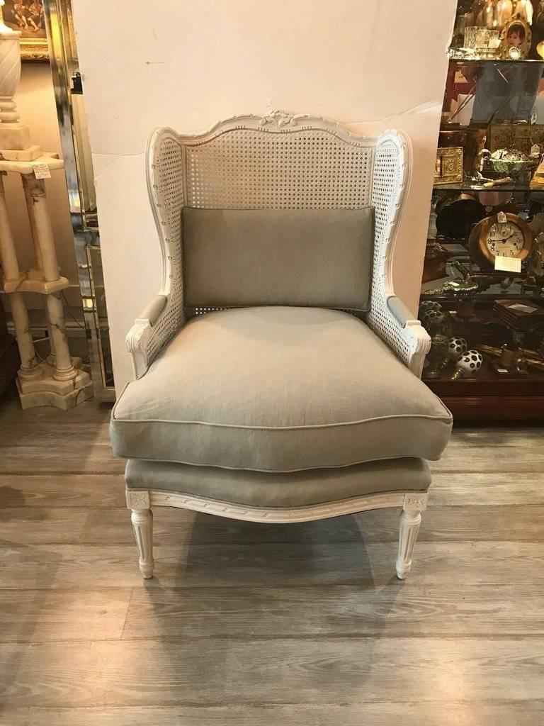 A pair of very stylish painted carved walnut wing chairs with caned backs and sides. The carved frames have detailing along the top sides and arms and rest on carved tapered legs. The new fabric is a cotton linen blend in a light gray color.
 