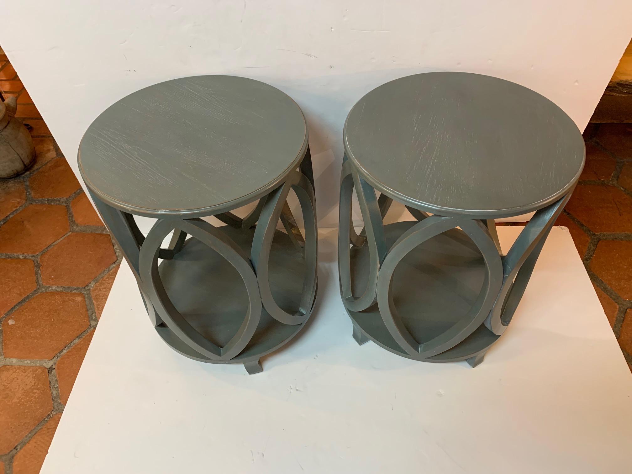 Stylish pair of painted wood round end tables in a slate gray blue, having sophisticated pointed oval shapes on the outside periphery and a lower tier.
