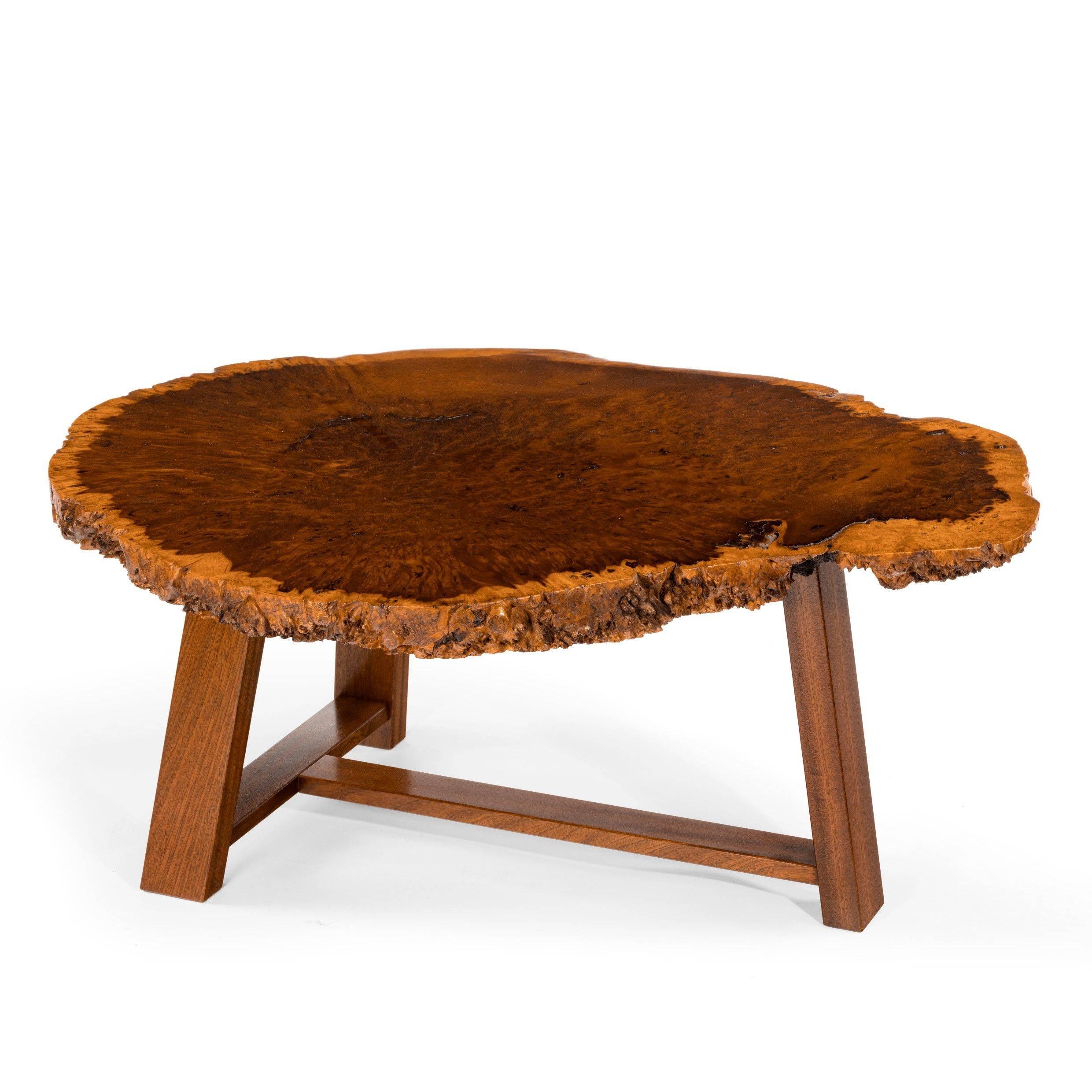 A stylish polished coffee tabletop, of irregular shape cut across the grain to show a central burr surrounded by a wide outer border of paler
wood, set on a modern base.