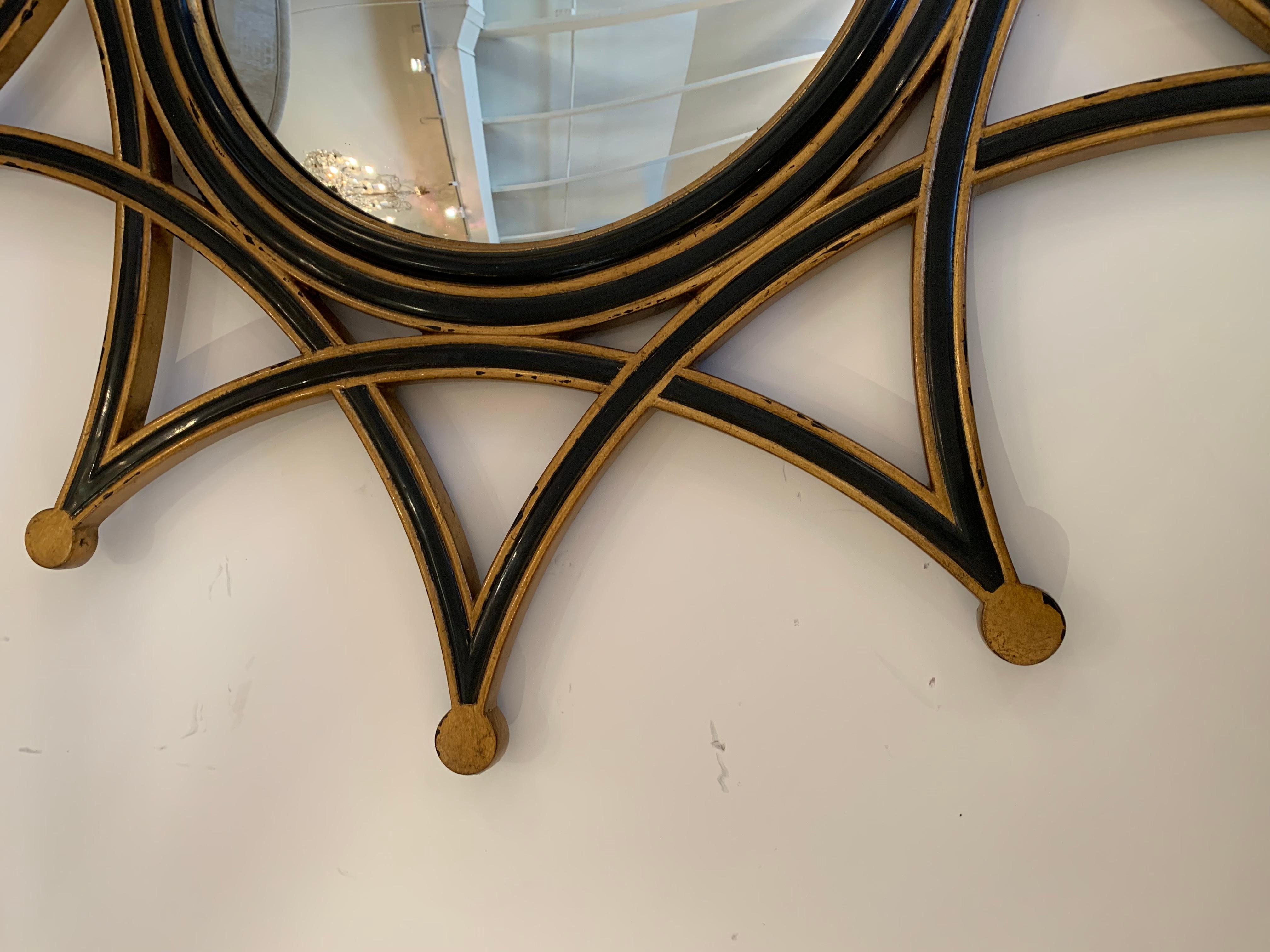 A contemporary starburst mirror by Theodore Alexander having black and gold frame with convex round mirror.