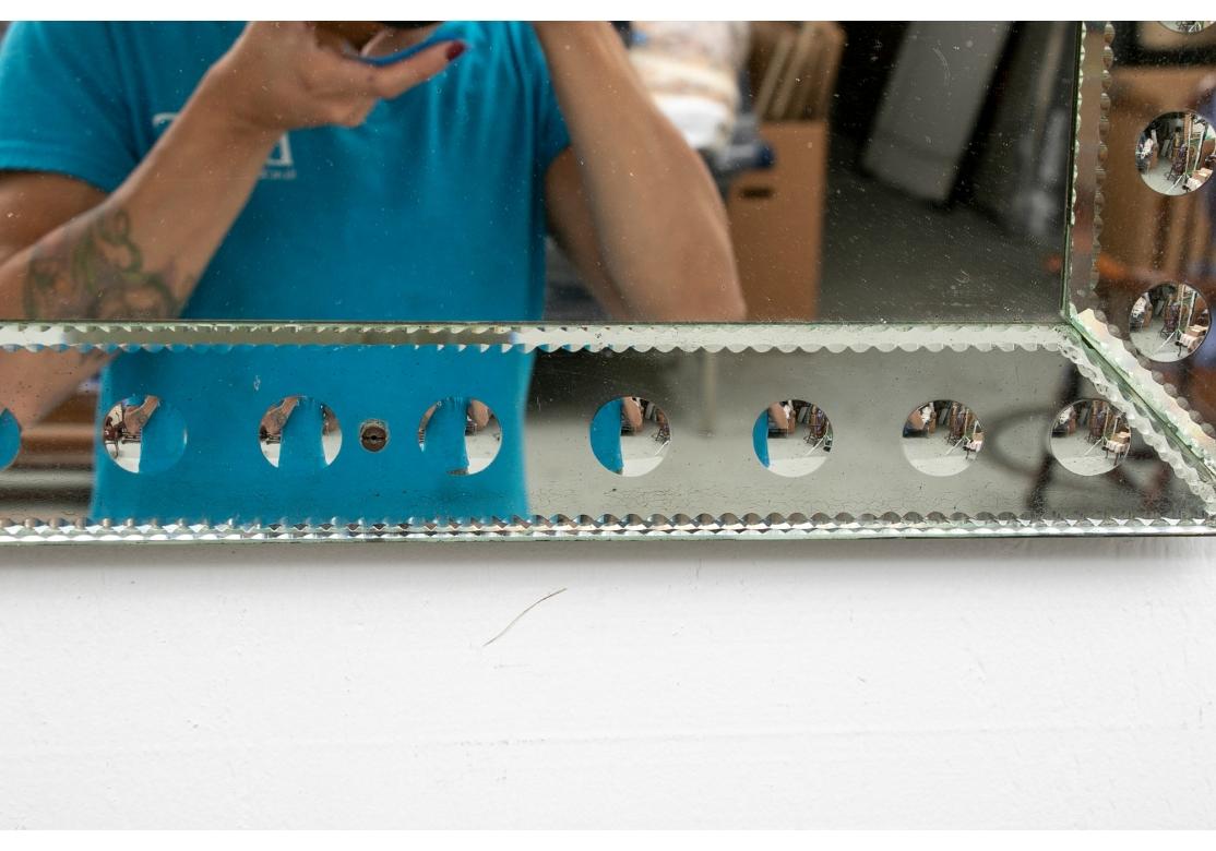 A 1970’s Optic effect mirror with segmented sections. The mirror surround assembled from four etched panels. Each with fine scalloped edges and bubble like circles. The panels attached to a wood frame backing with tiny glass rosettes (lacking the