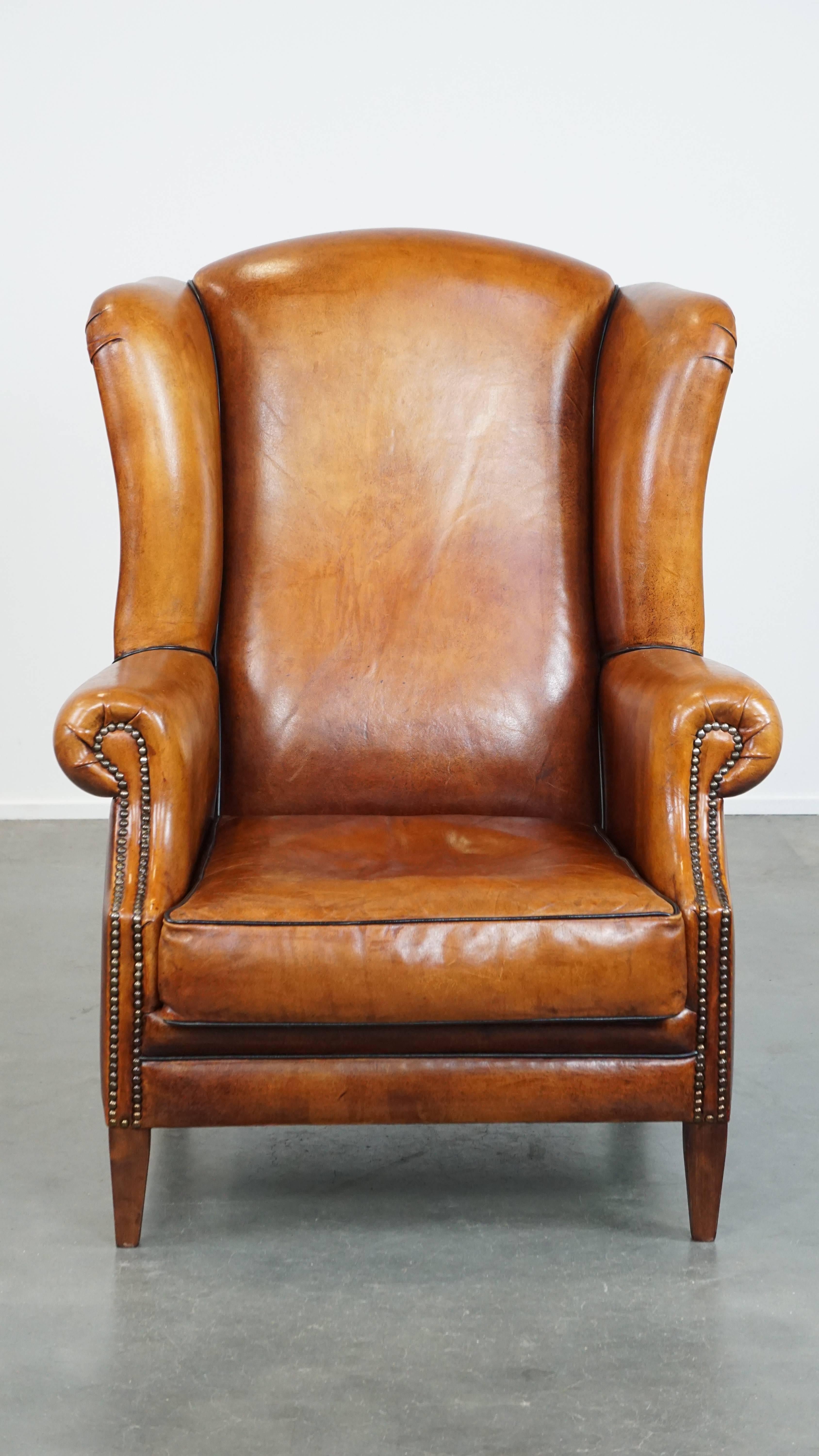 Ce fantastique fauteuil à oreilles en peau de mouton est un joyau intemporel qui s'intégrera dans presque tous les intérieurs. Sa couleur chaude, sa finition avec des passepoils noirs et des clous décoratifs, et son assise généreuse en font