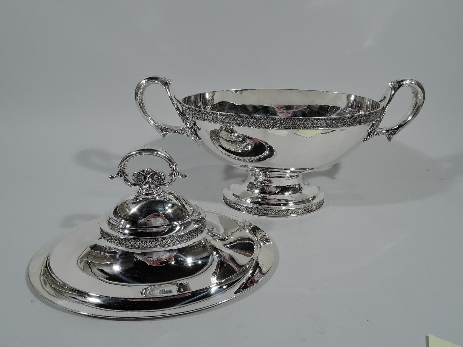 Stylish sterling silver tureen with stylized ornament. Made by Tiffany & Co. in New York. Curved and oval bowl on raised oval foot. Dynamic capped loop handles with split foliate mounts. Stepped and domed cover has leaf-capped and scrolled ring