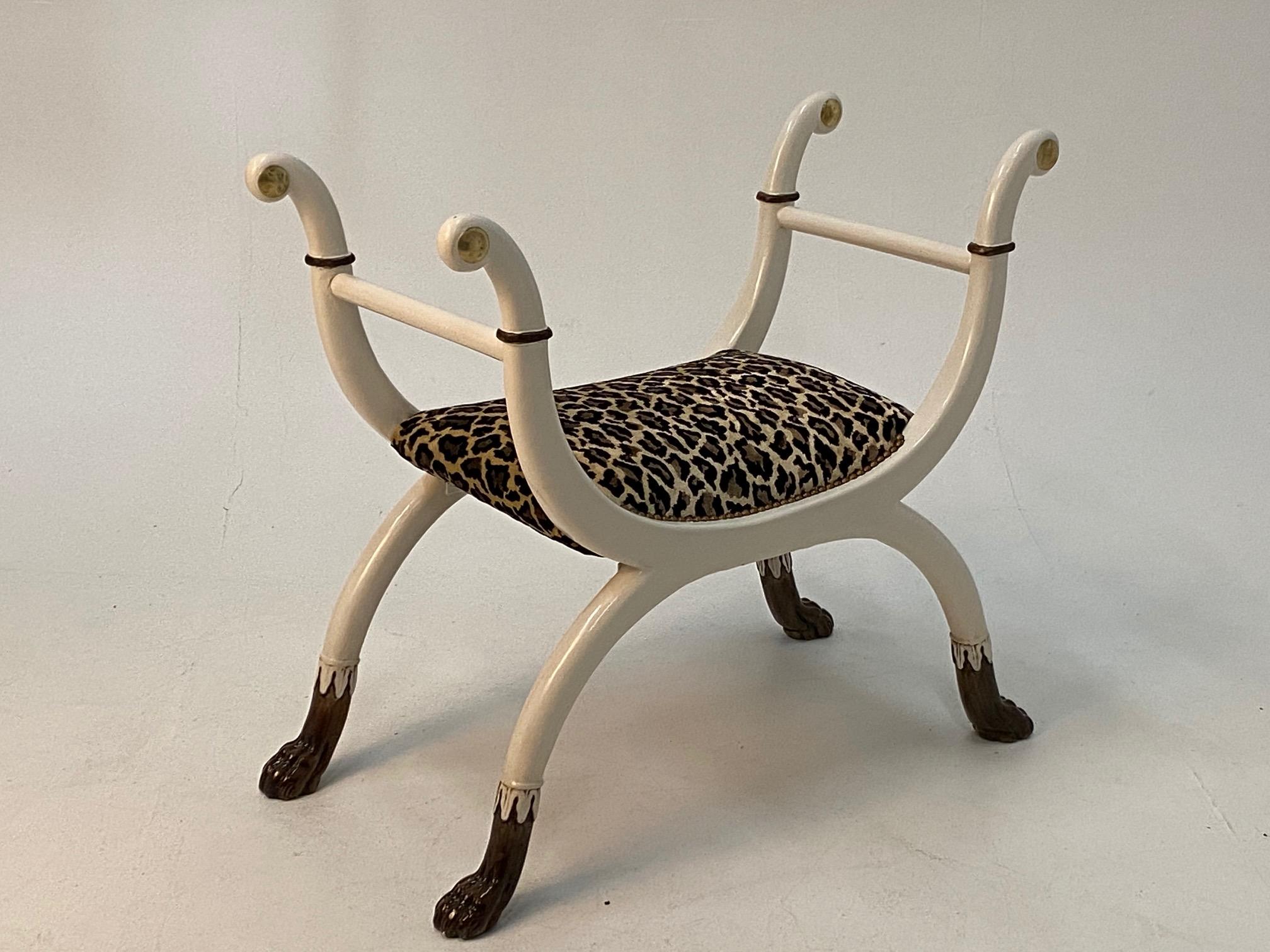 Super chic Regency style bench having white lacquer wood with black and brass accents and sensual curvy shape. Seat is newly upholstered in complimentary faux leopard fabric and the legs terminate in wonderful black lacquer paw feet.