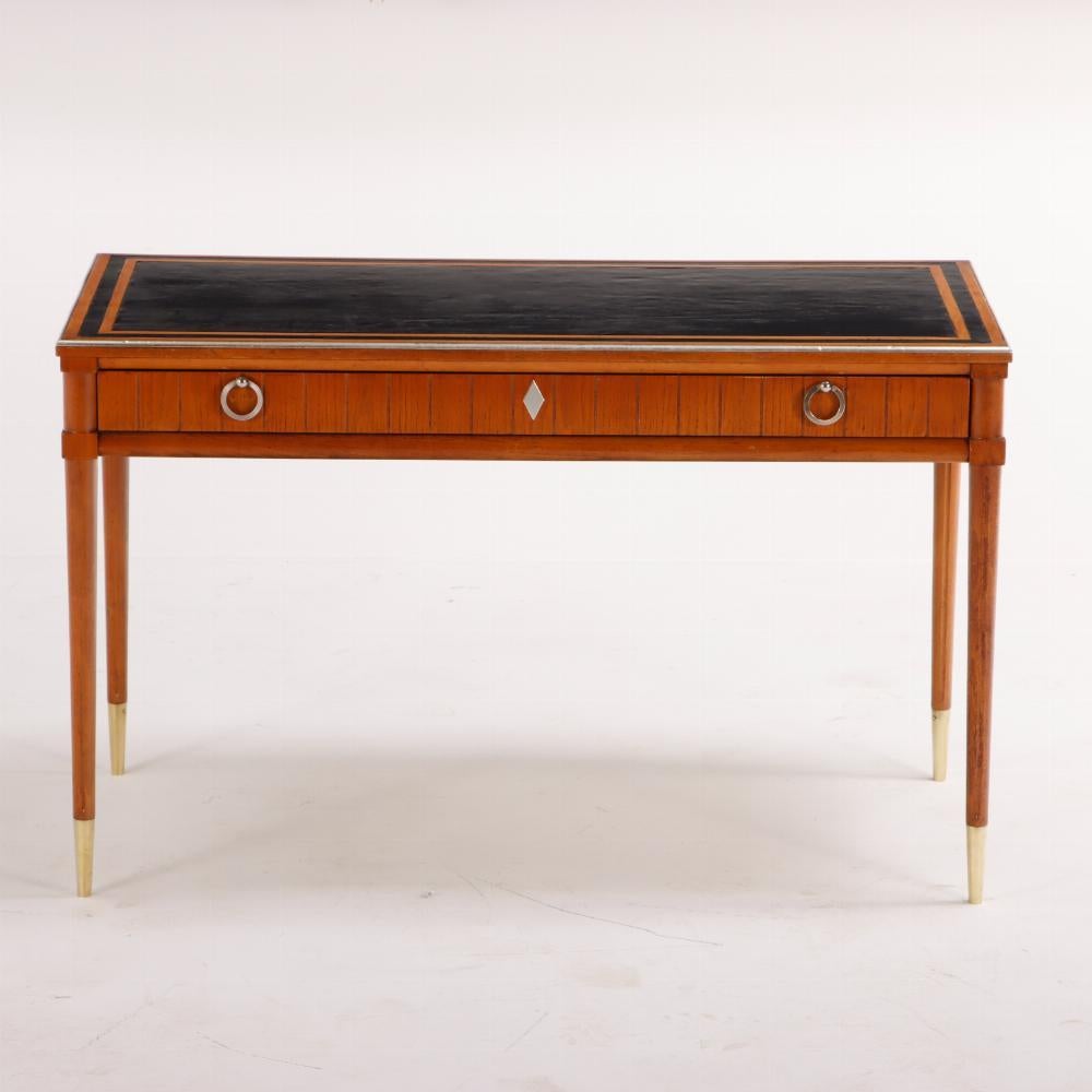 Stylish leather top walnut writing desk in the manner of Jean-Michel Frank C 1960 having a black leather writing surface over a with single drawer,  bronze hardware, and turned legs.