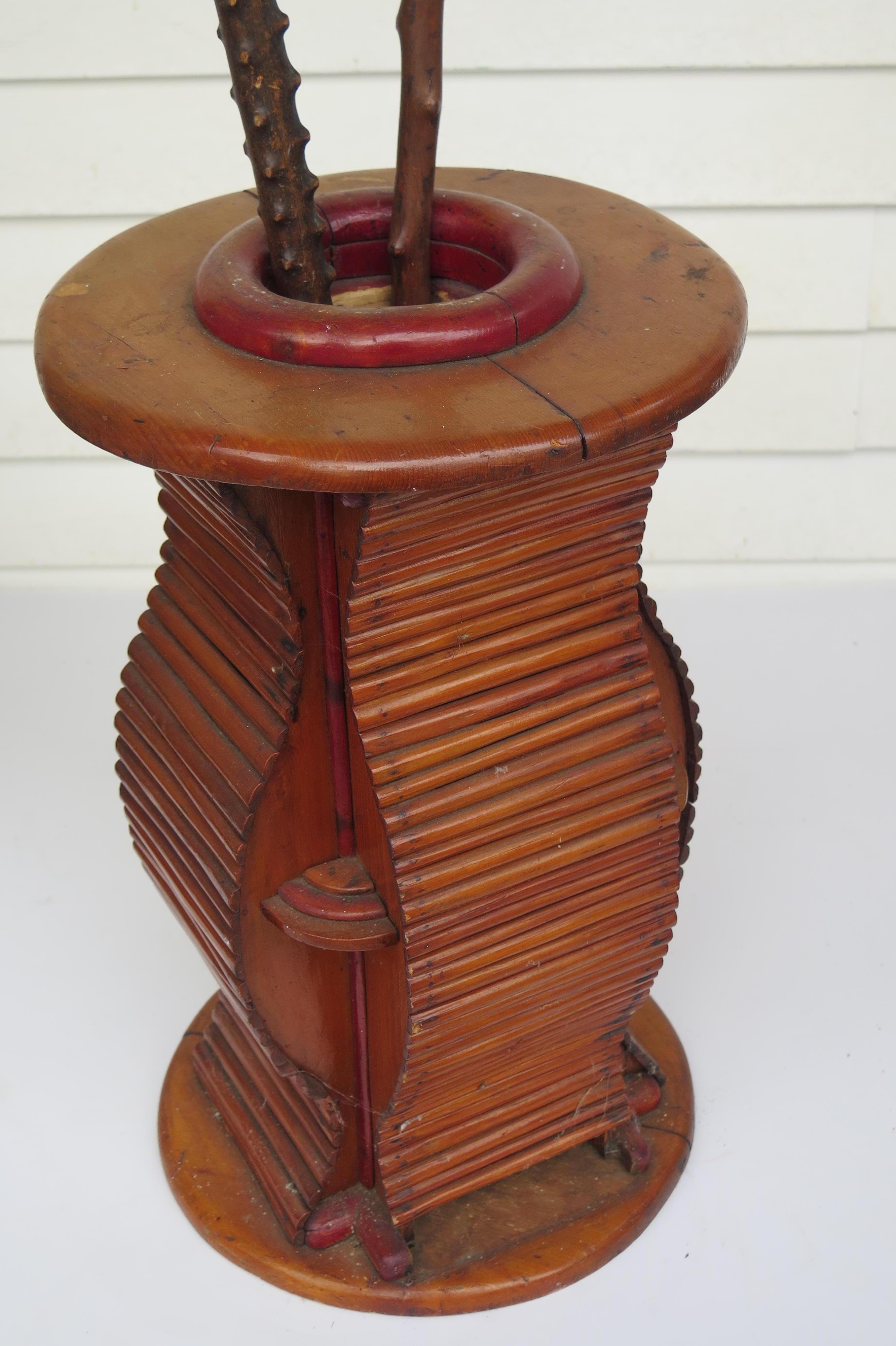 Deco period cane stand of pieced wood. Undulating form on 4 sides of half round wood with quarter discs between the sides. 
Red stained ring opening on larger disc top and disc bottom. The lightly stained wood has a varnish coat finish.