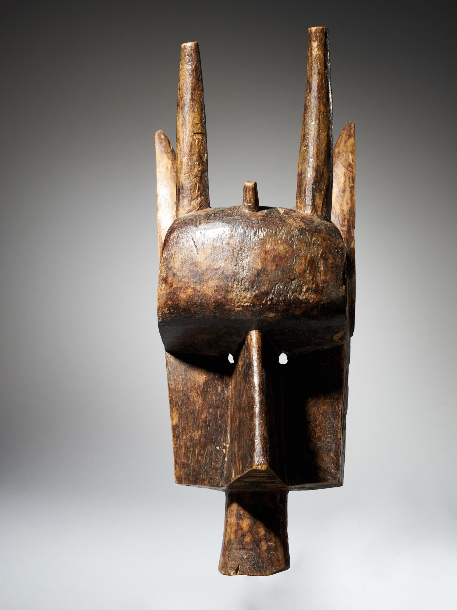 This wooden mask is made by the Bamana Kore society in Mali. It has very pronounced features, like the long, straight nose and the broad forehead protruding from the mask. Next to the nose are small circular holes for the eyes and beneath the nose