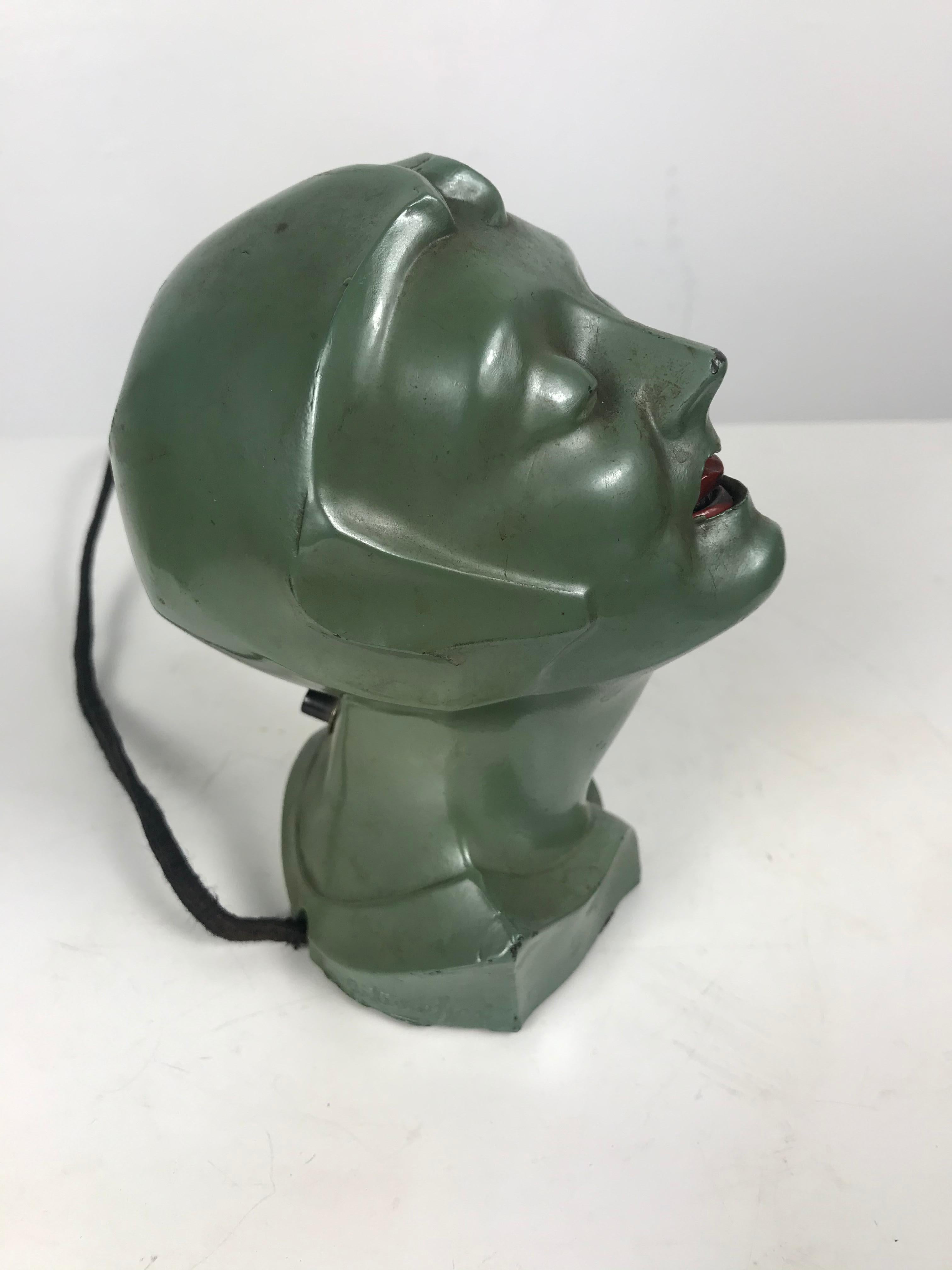 Stylized 1930s Art Deco women's head electric cigarette lighter by Arturo Levi. Retains original paint, finish, as well as original electrical plug and push button that heats up coil in women's mouth. Minor dent and paint loss to back of head,