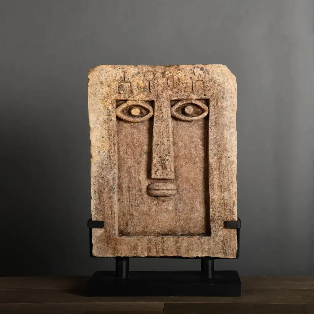 Le modèle Ideograms est une stèle iconique en grès naturel, inspirée des piliers archéologiques de l'ancien royaume de Saba au Yémen. Fabriqué à la main, il présente un visage frontal raffiné avec un nez droit, de fortes arcades sourcilières, des