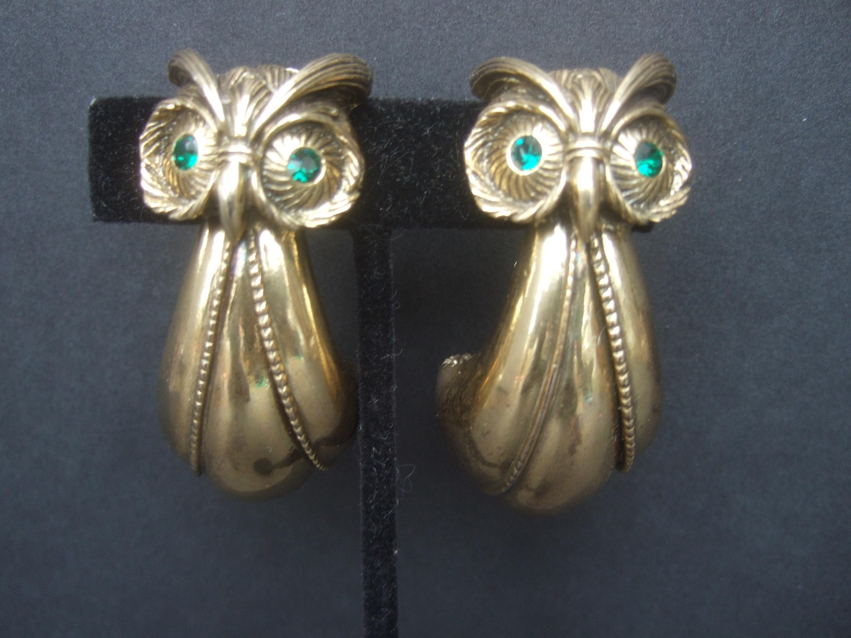 Stylized large scale gilt metal clip-on owl earrings c 1970s
The unique figural statement earrings are designed with a pair
of endearing owls 

Embellished with green crystals eyes. The sleek gilt metal plating
is accented with impressed & etched