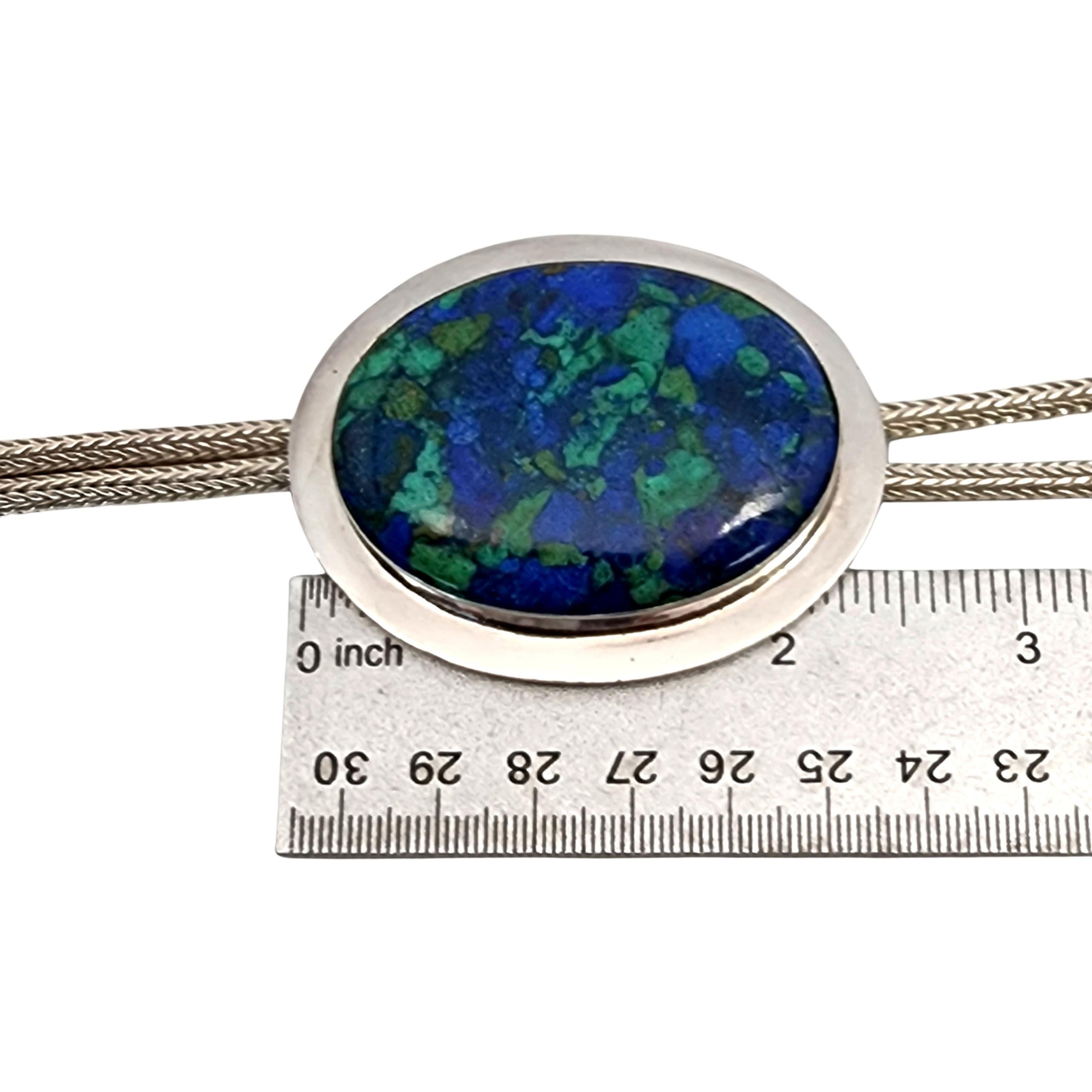 Sterling silver azurite malachite bolo tie by Suarti.

This handcrafted artisan piece features a round woven chain with cylinder tips. The large beautiful oval shaped azurite malachite stone is bezel set in the highly polished bolo focal