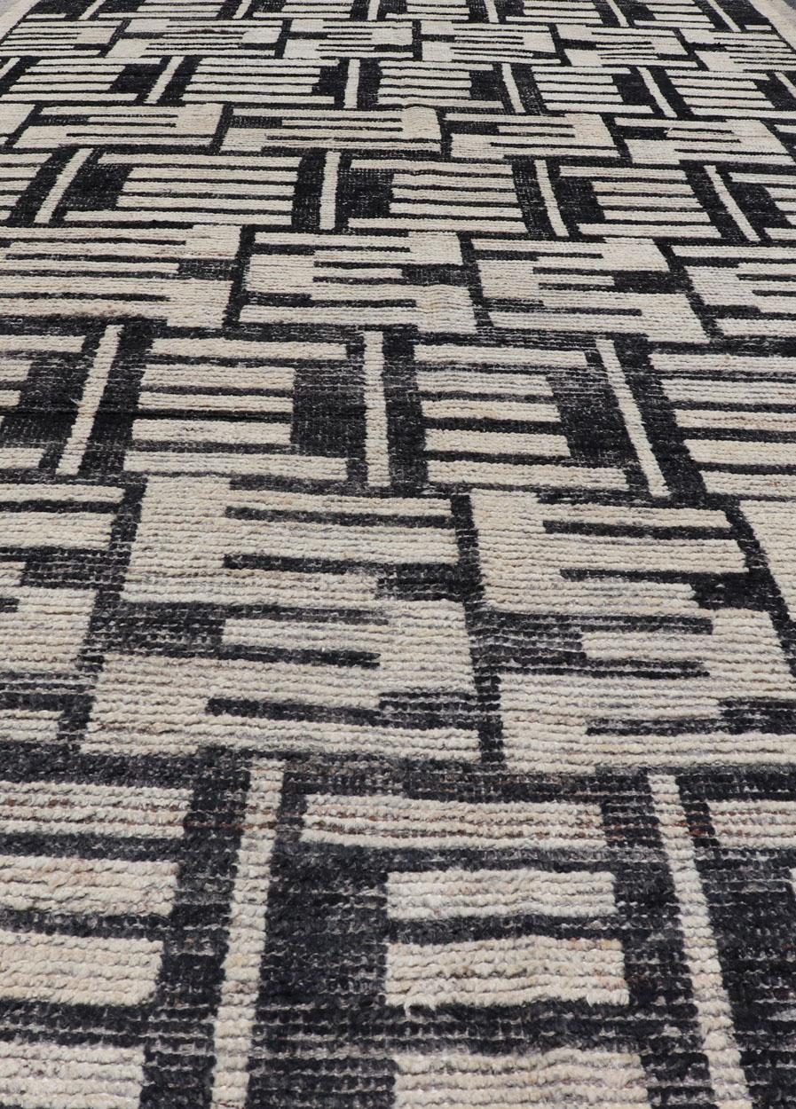 This Afghan hand-knotted area rug features an abstract, all-over design in ivory. The background is rich with ebony, while the design and border each display shades of ivory and bone. This modern treasure is simple and sophisticated, making this
