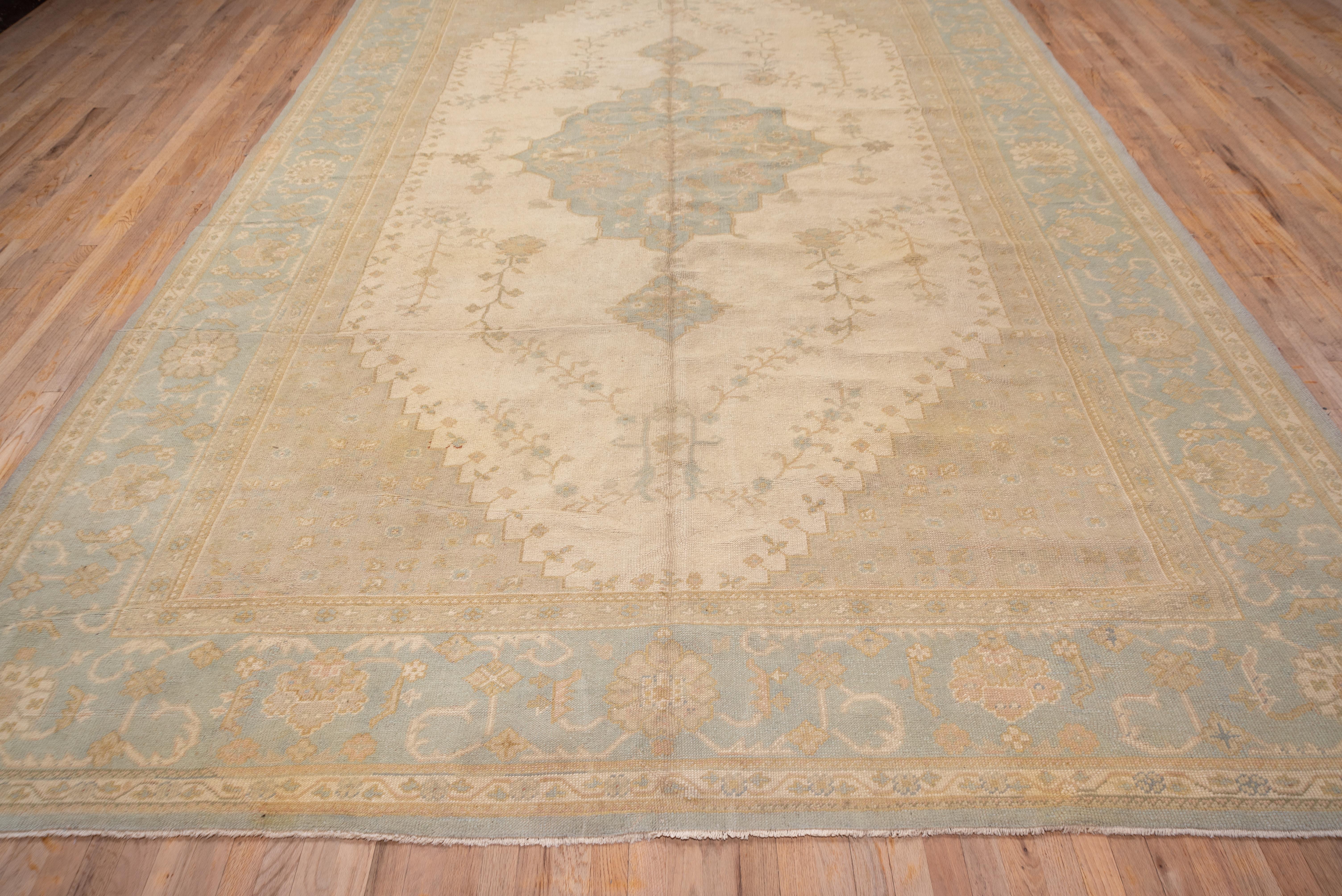 This west Anatolian town carpet is a subdued study in ivory, and very pale green. The cream subfield is edged with small flowers and centres a lobed, pendanted and pointed medallion. The palest green border displays corner rosettes, palmettes and