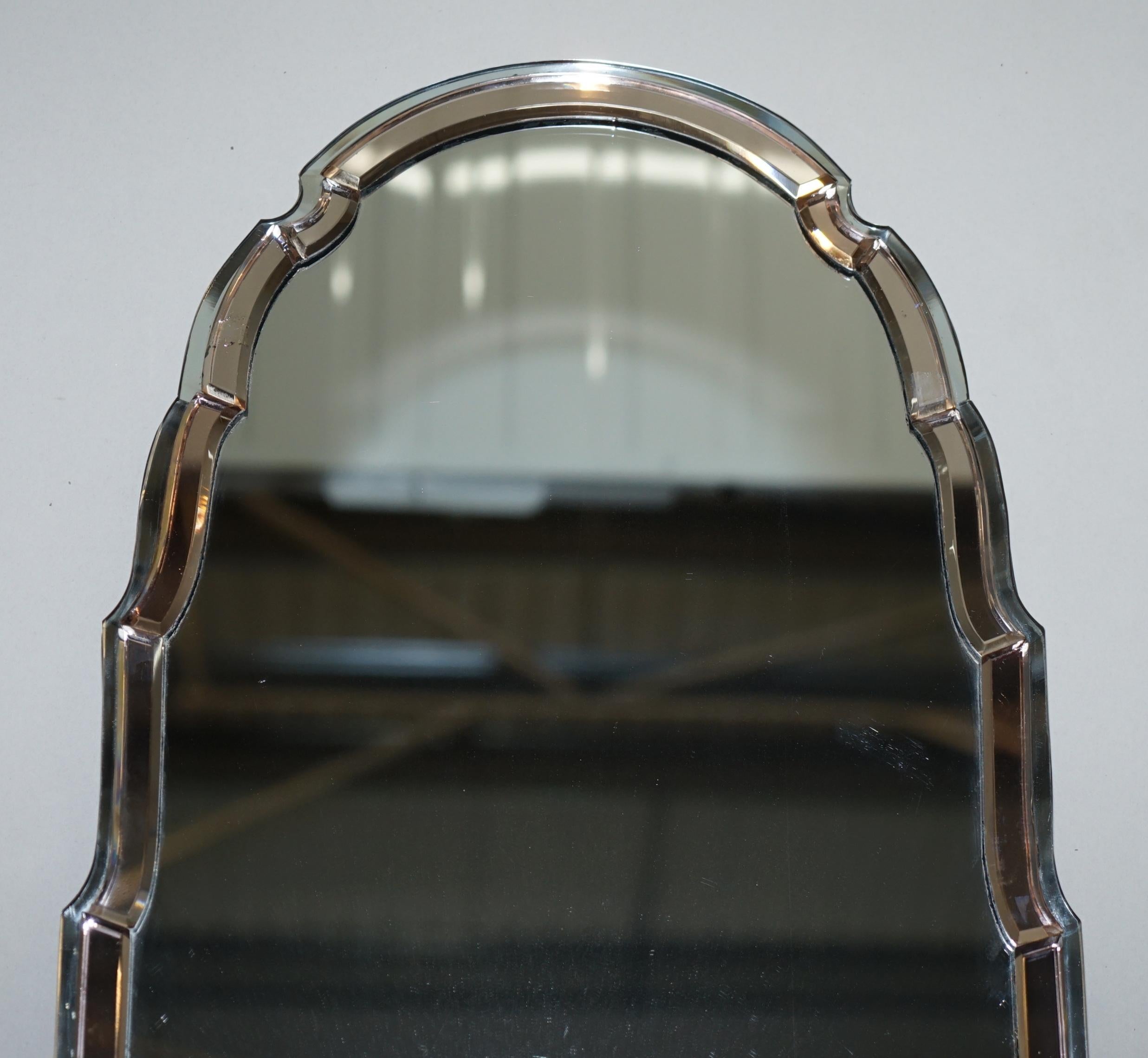 Nous sommes ravis d'offrir à la vente ce superbe et exceptionnellement rare miroir vénitien en verre pêche Art déco des années 1930, avec un cadre à bord biseauté et un sommet courbé en forme de clocher. 

Un très beau miroir mural bien fait et