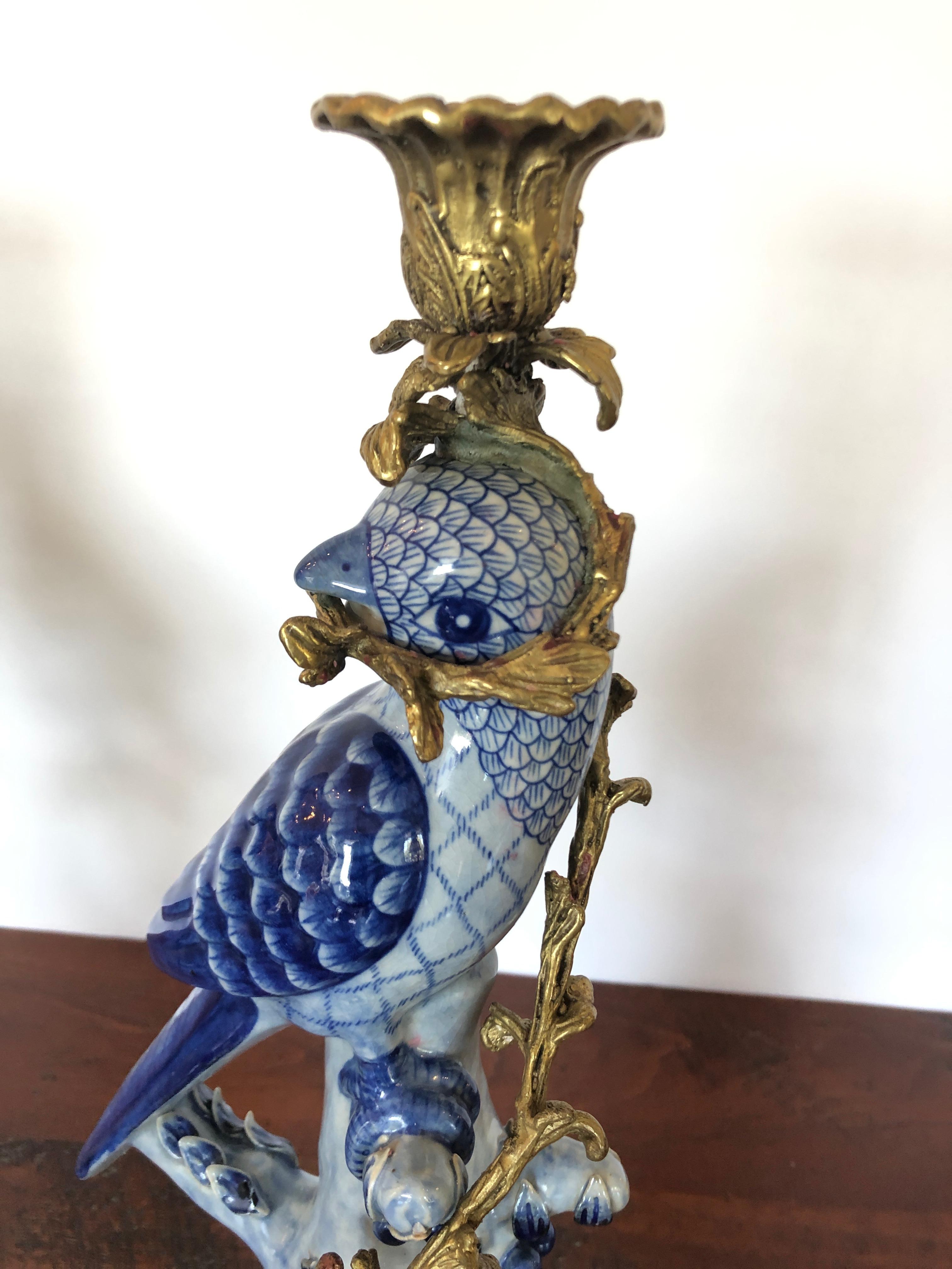 An incredible ornate pair of blue two tone porcelain parrot candlesticks having bronze bases, candle cups and faux bois vines around the body of the objects.