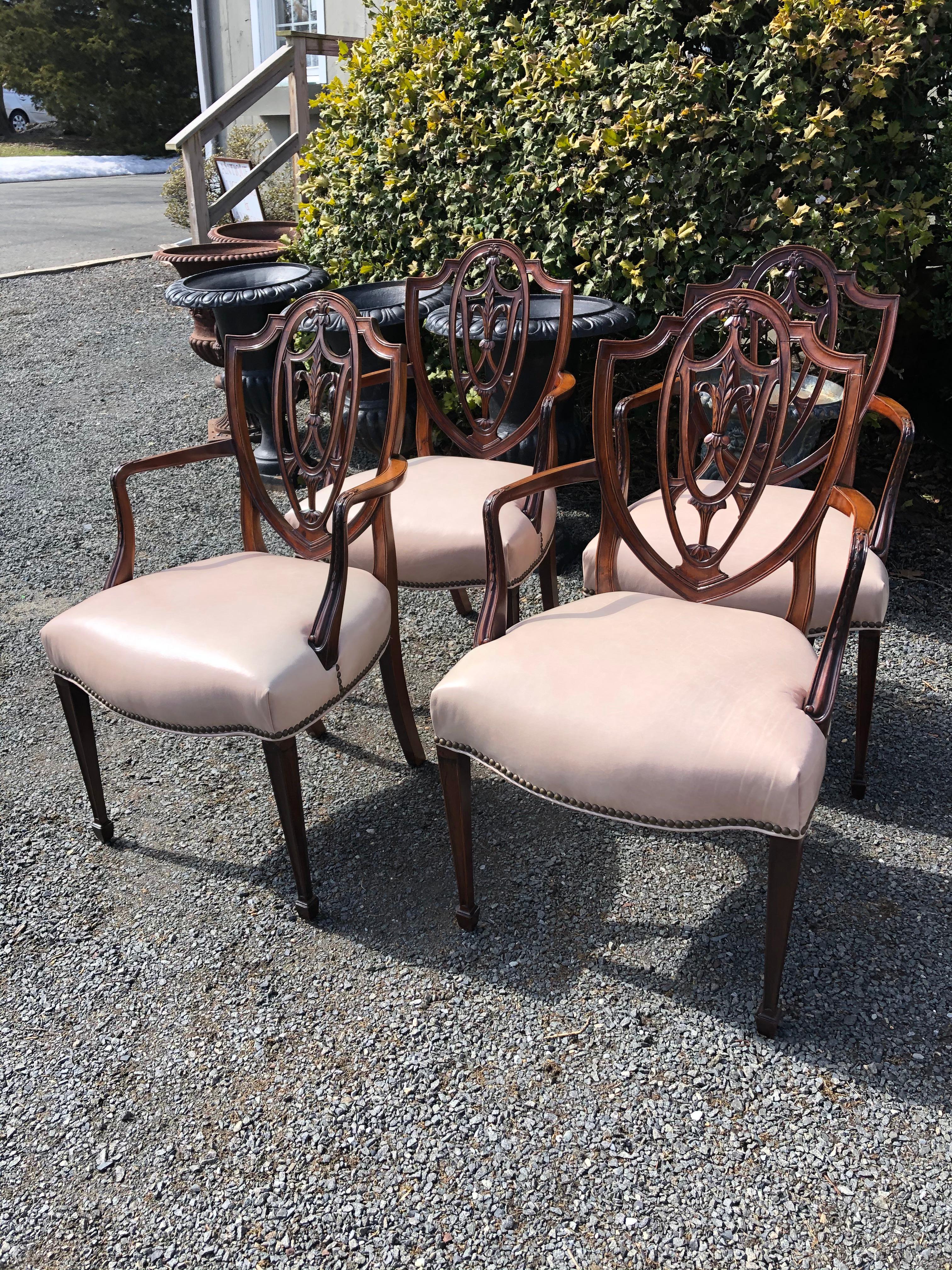 Utterly sublime and refined set of 4 elegant antique mahogany armchairs having carved wood shield backs, delicate curved arms and tapered legs, updated with glamorous blush leather seats finished with nailheads. 
Measures: Seat height 18
Arm