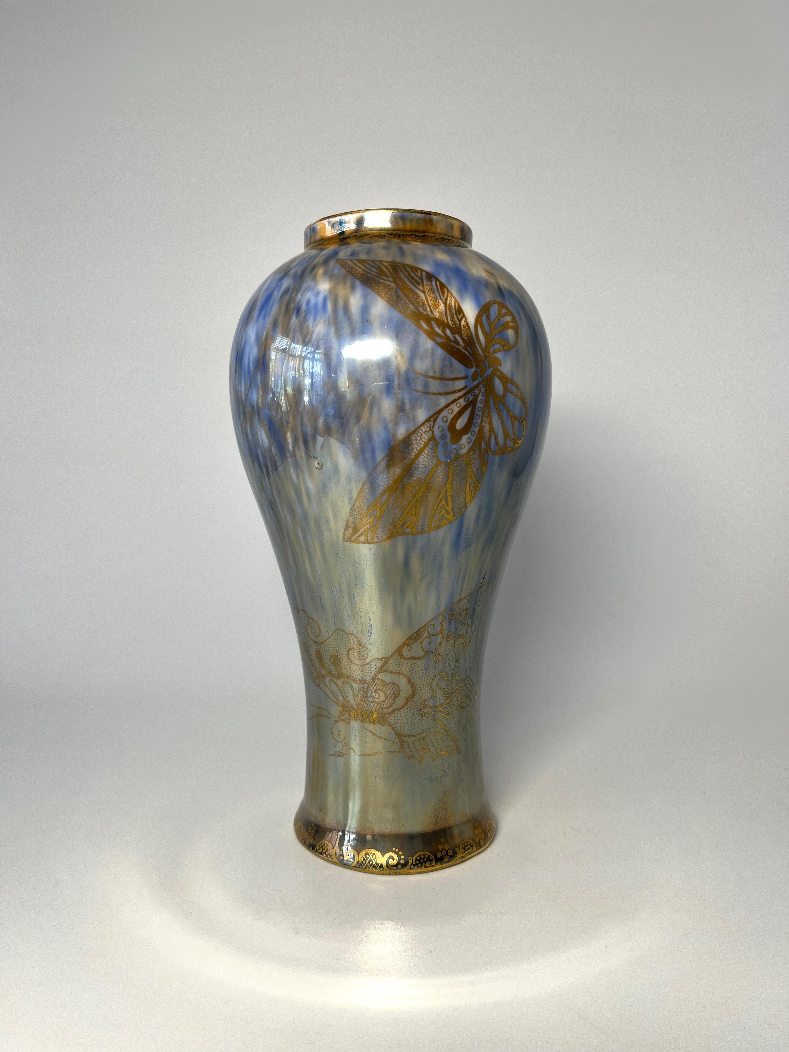 Uno splendido vaso Wedgwood con uno smalto che ricorda una sottile tela di seta. Il fondo blu cielo ha un velo di screziatura marrone dorata, ornato da uno svolazzo di farfalle dorate.
Un'intricata filigrana dorata decora i bordi superiore e