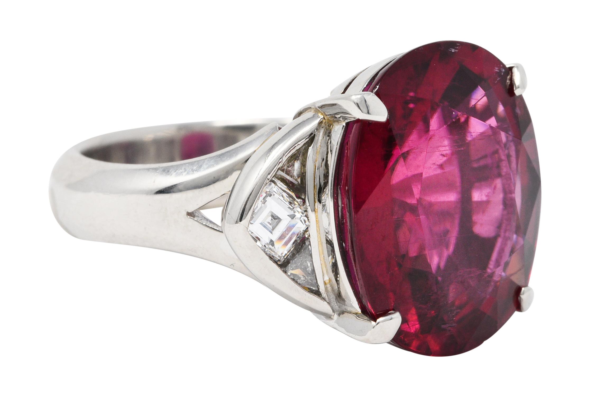 Substantial gemstone ring centers an oval cut rubellite tourmaline

Weighing 12.84 carats with strong and uniform raspberry red color

Basket set and flanked by stylized navette shoulders

Set with square step and triangular cut diamonds

Weighing