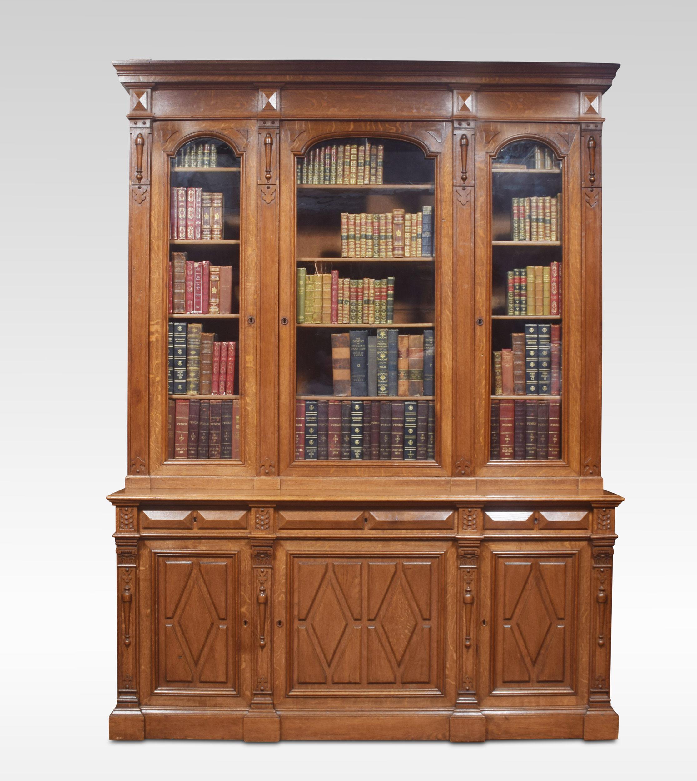 A substantial 19th century oak bookcase, the moulded cornice with geometric applied detail above three large glazed doors enclosing adjustable shelved interior. To the base having three freeze draws and three carved cupboard doors below. All raised